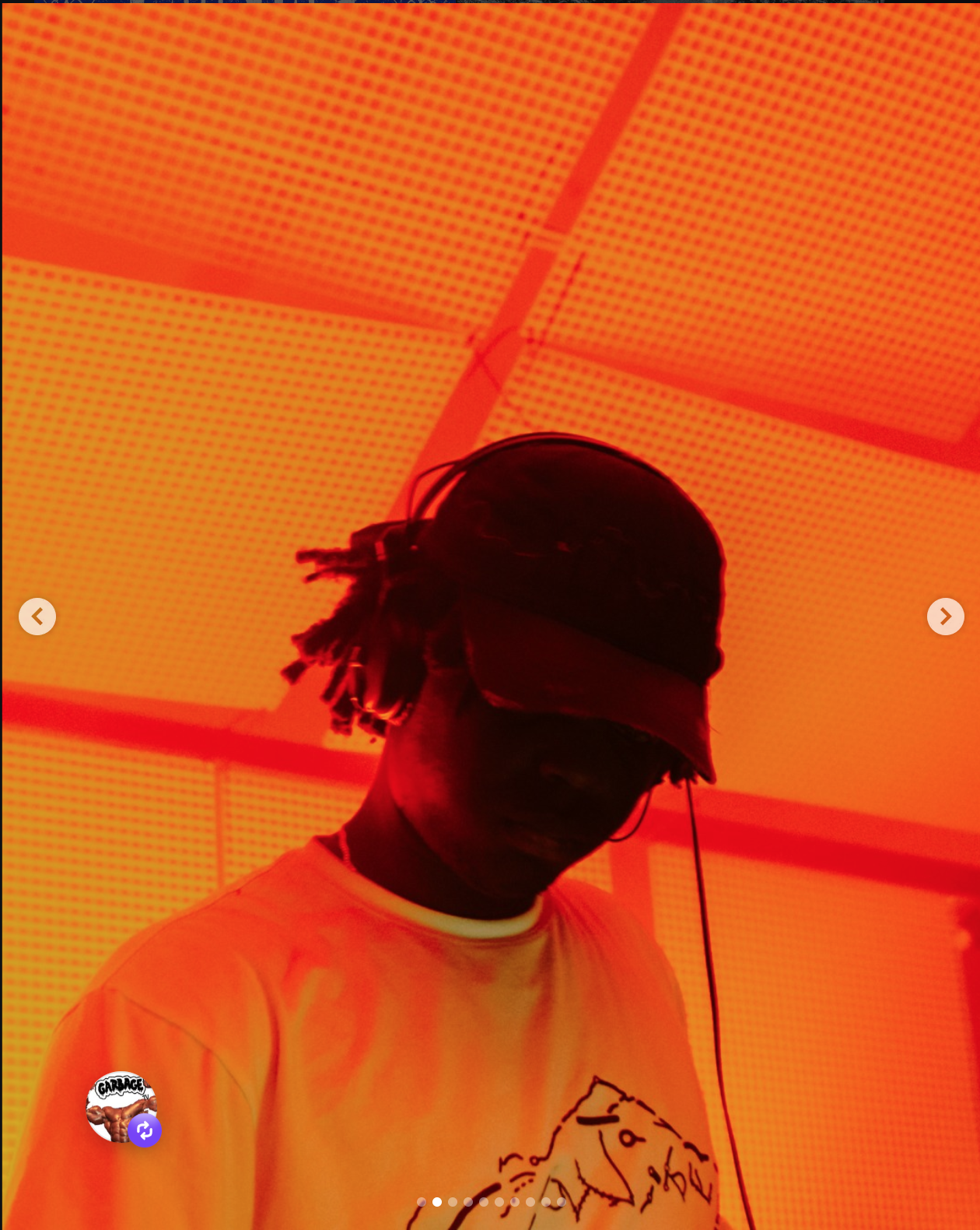 A person wearing a black cap, sunglasses, and a mask, standing under an orange-lit ceiling with perforated panels.