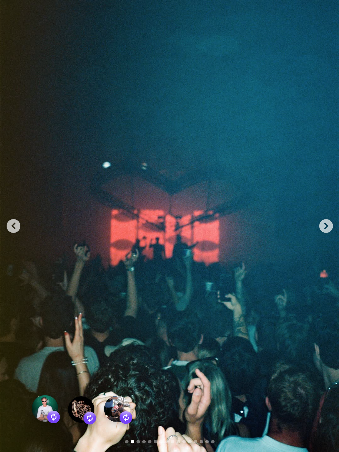 A crowd of people at a concert or nightclub, raising their hands and dancing in front of a stage with red lighting and silhouettes of performers.