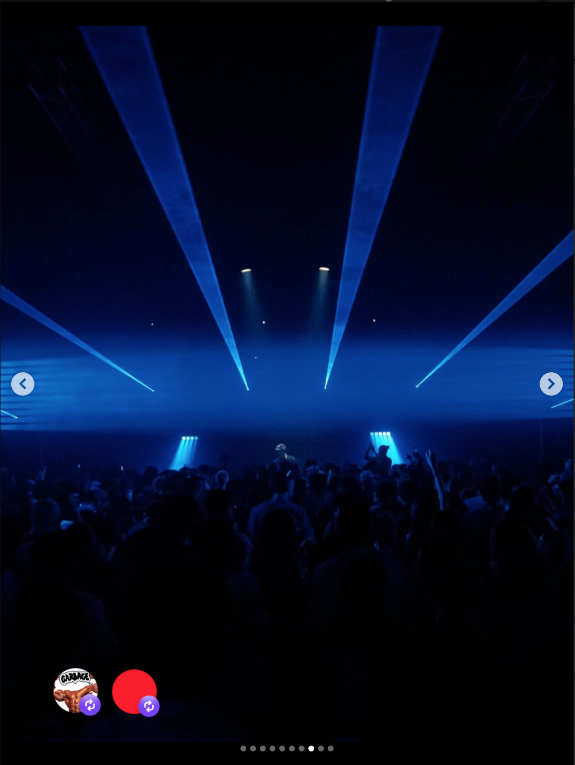 A concert scene with blue laser lights shooting down from the ceiling, silhouetted crowd dancing, and a DJ or performer on stage.