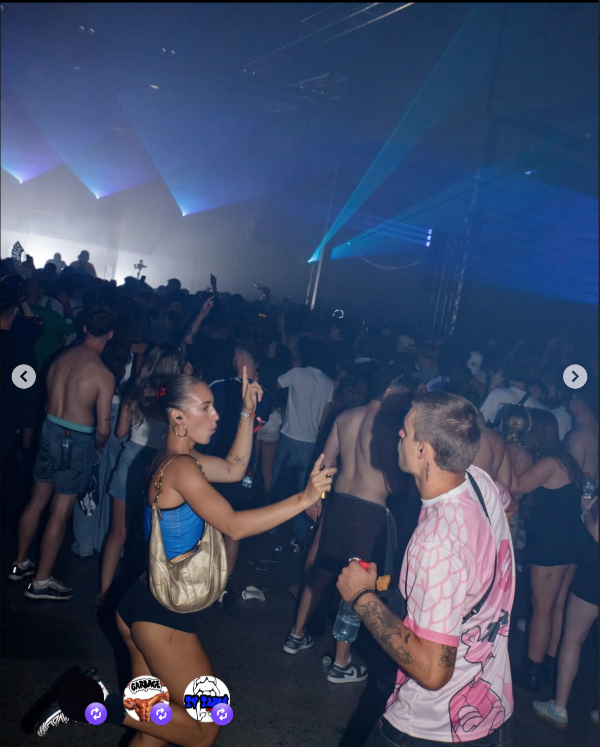 Crowd of people dancing at a nightclub with laser lights and fog, some making gestures and taking photos.