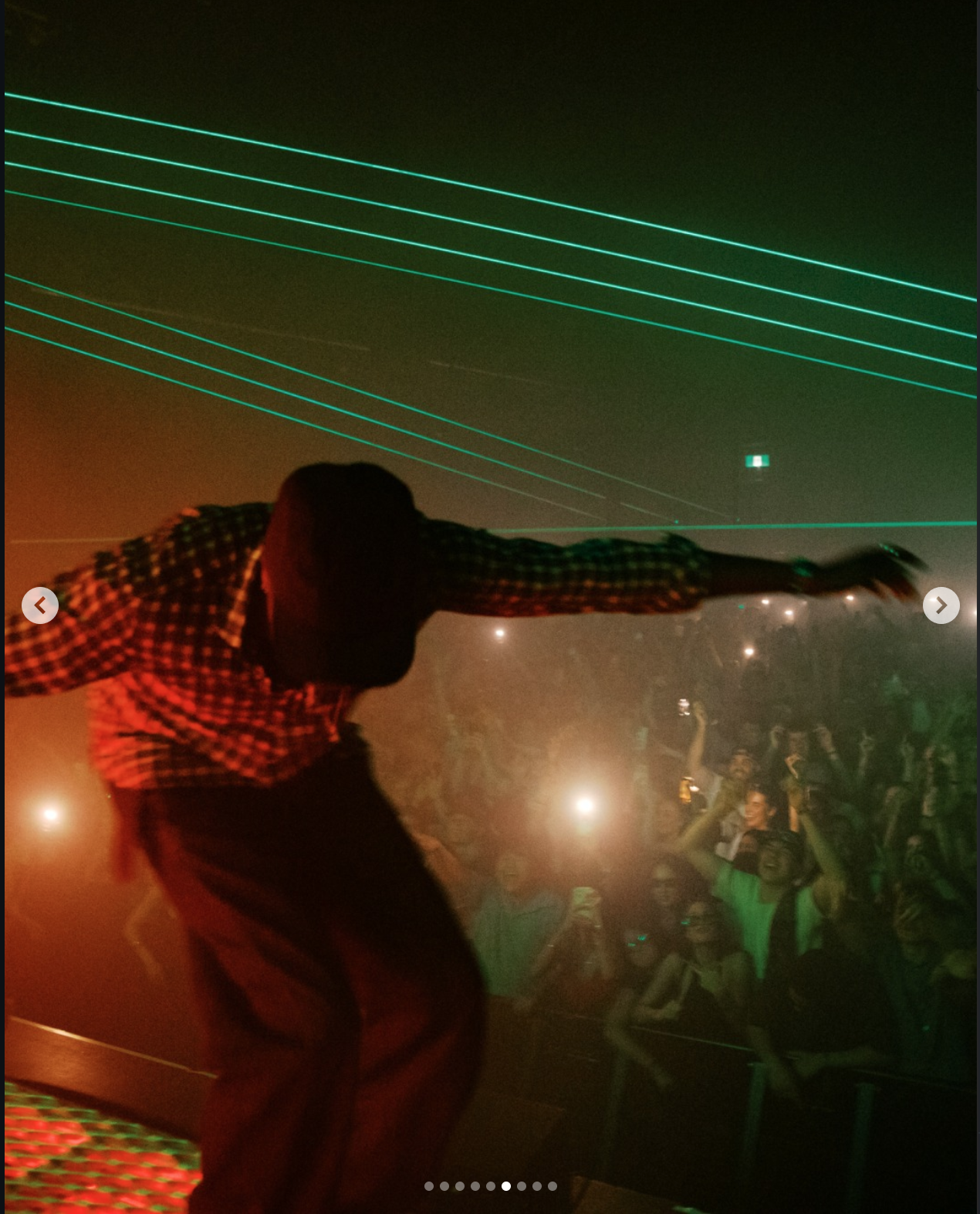 Person dancing on stage at a nightclub with laser lights overhead and a crowd enjoying the performance.