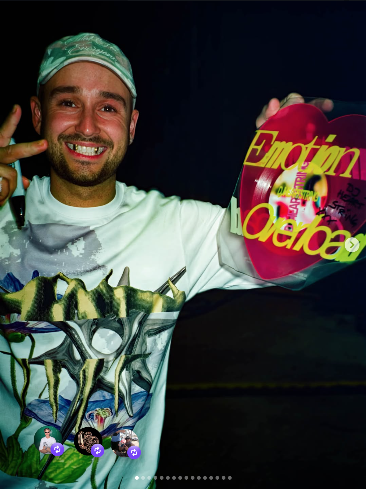 A smiling man wearing a baseball cap and white t-shirt holding a large transparent bag with a colorful design, and a heart-shaped object with the words 'Emotin' and 'Love' in bright yellow and pink letters, with signatures and messages written on it.