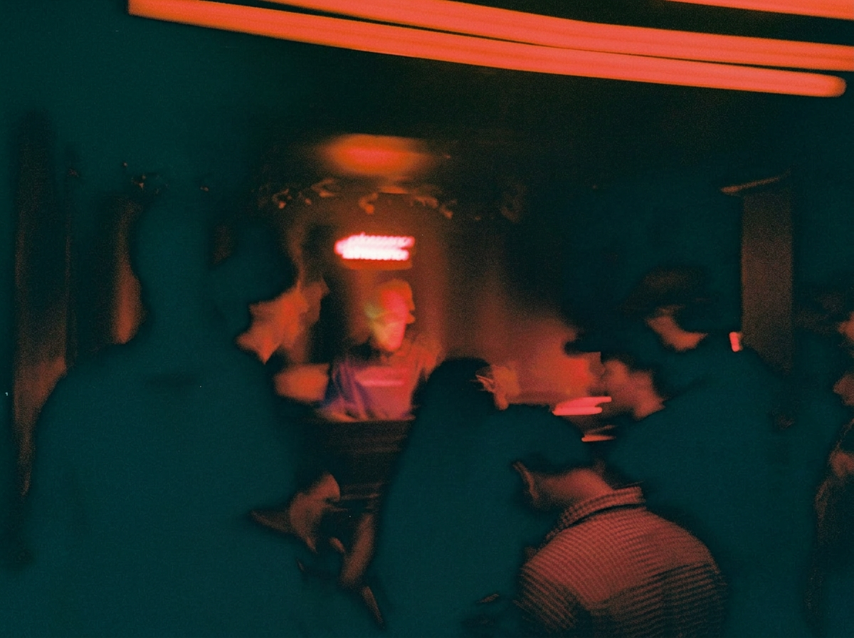 People gathered in a dimly lit bar or club with red neon lighting, engaging in conversation.