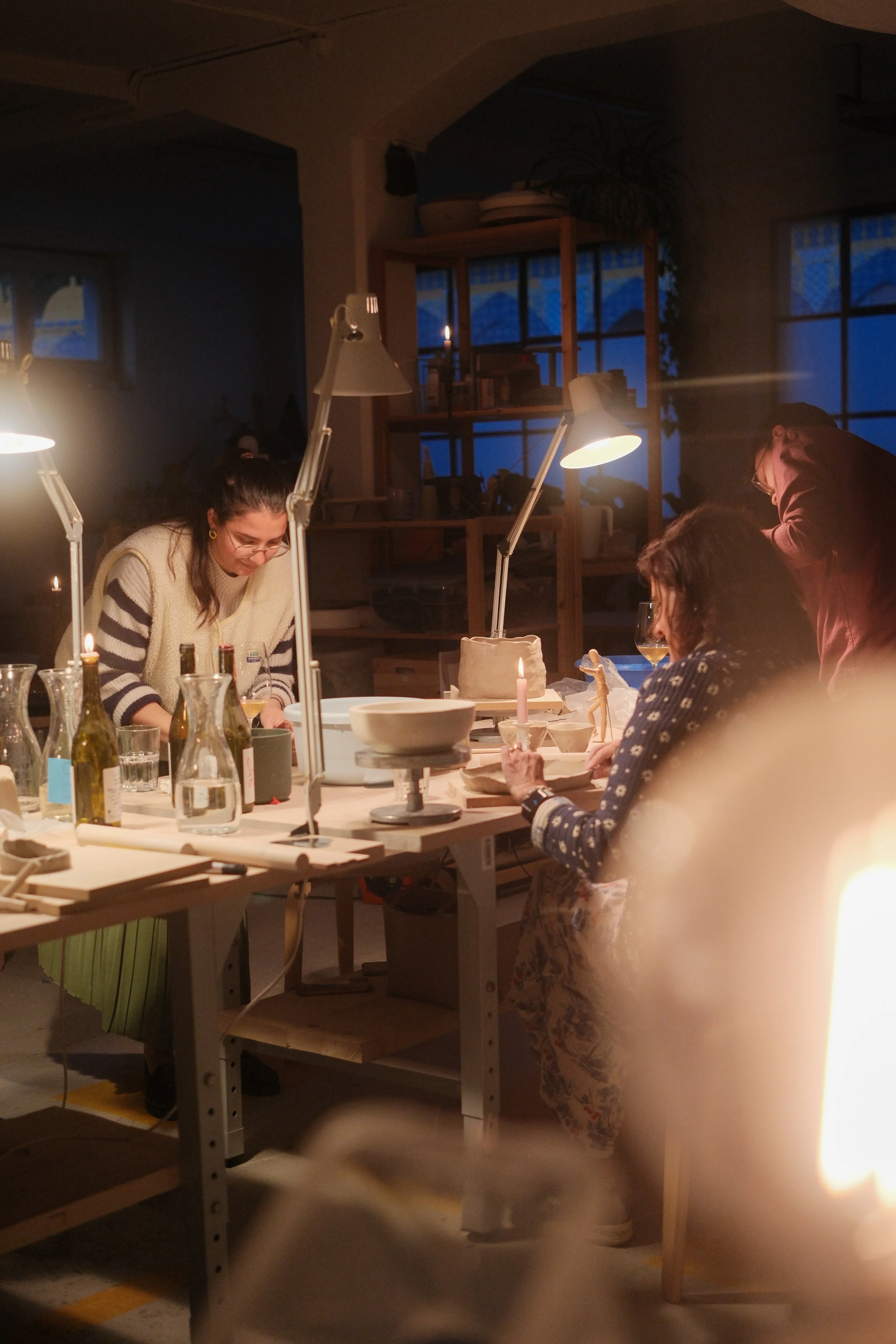 Menschen arbeiten in einer Werkstatt bei geschaltetem Licht, es ist dunkel draußen, Fenster im Hintergrund.