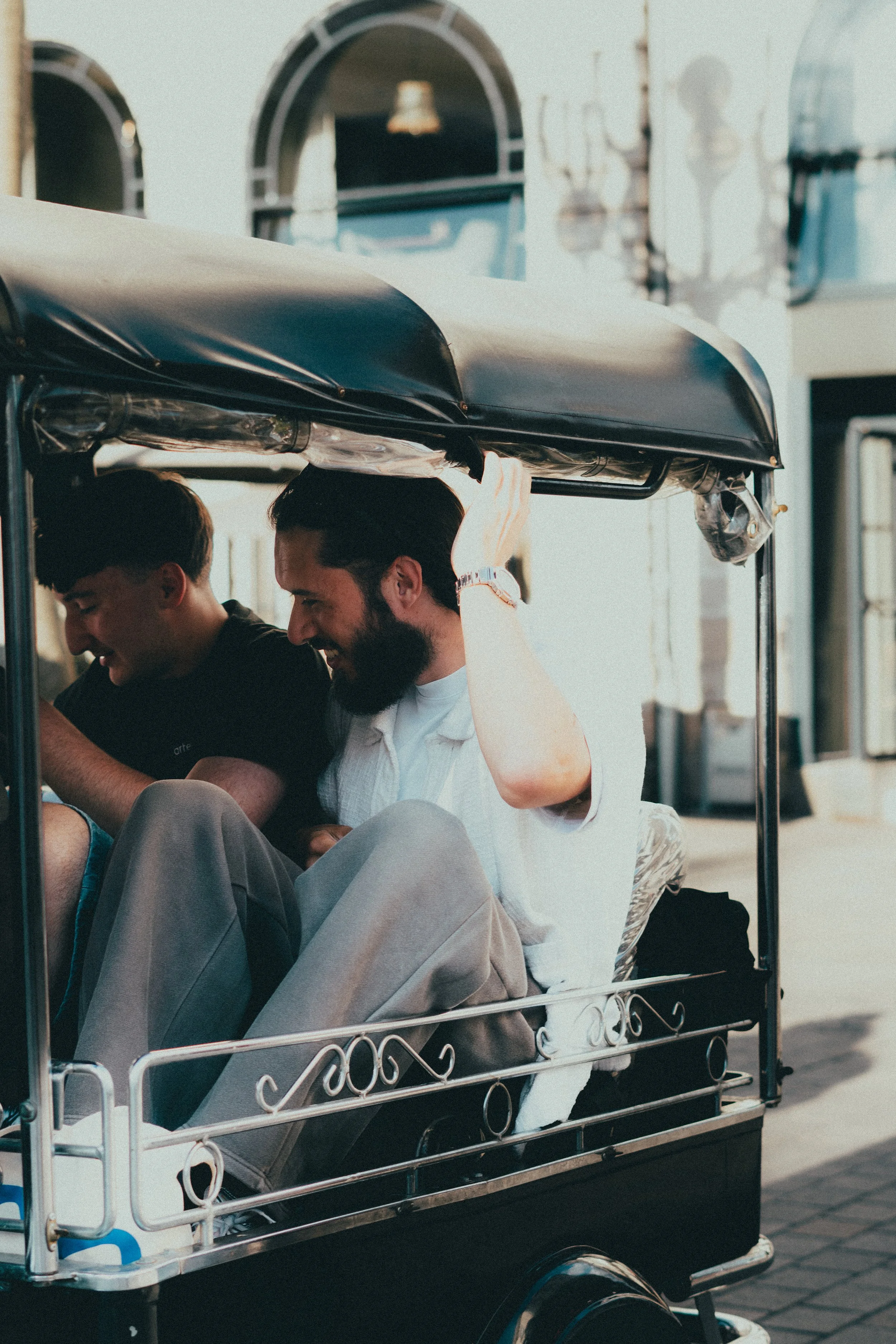 Deux hommes assis dans un pousse-pousse, riant ensemble lors d'une journée ensoleillée en ville.