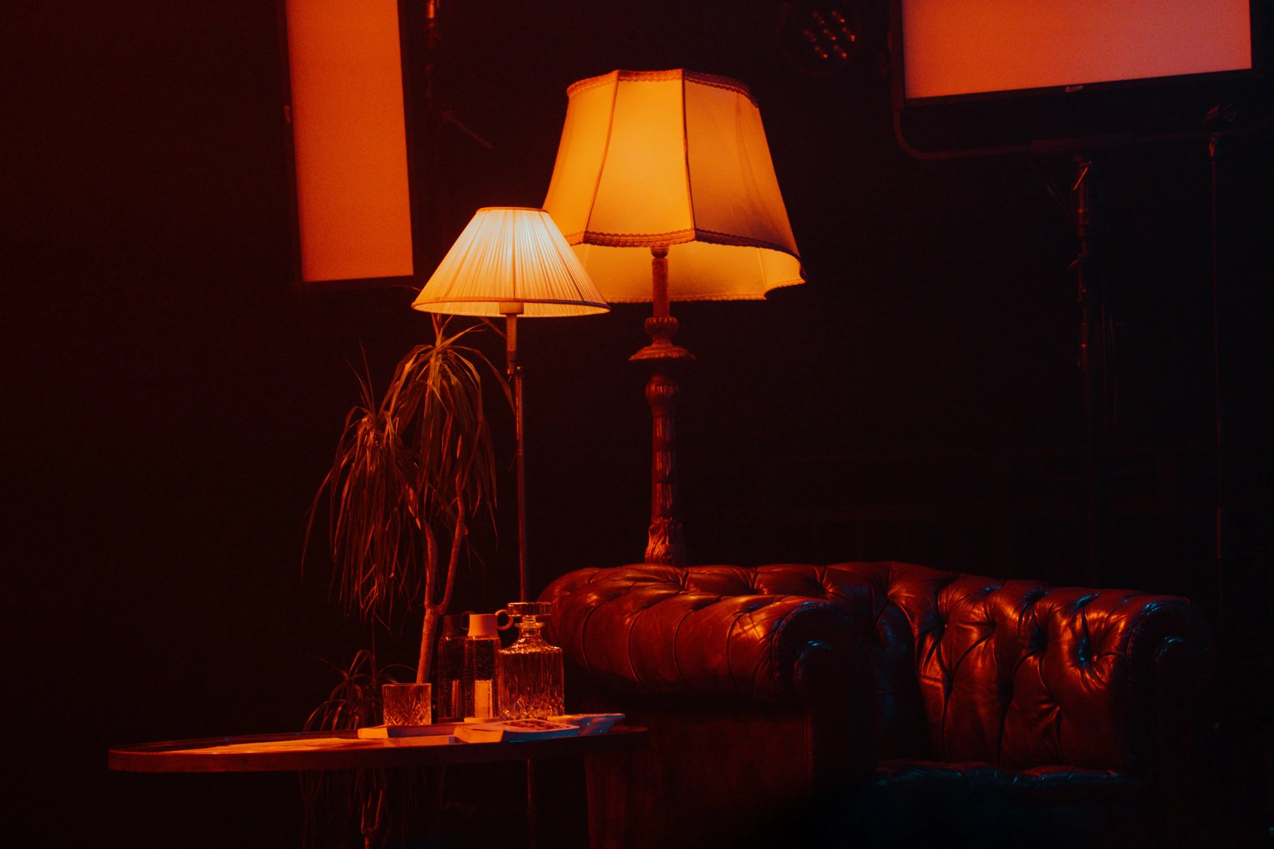 Lampe de salon chaude allumée, canapé en cuir, plante d'intérieur, bouteille en verre sur une table