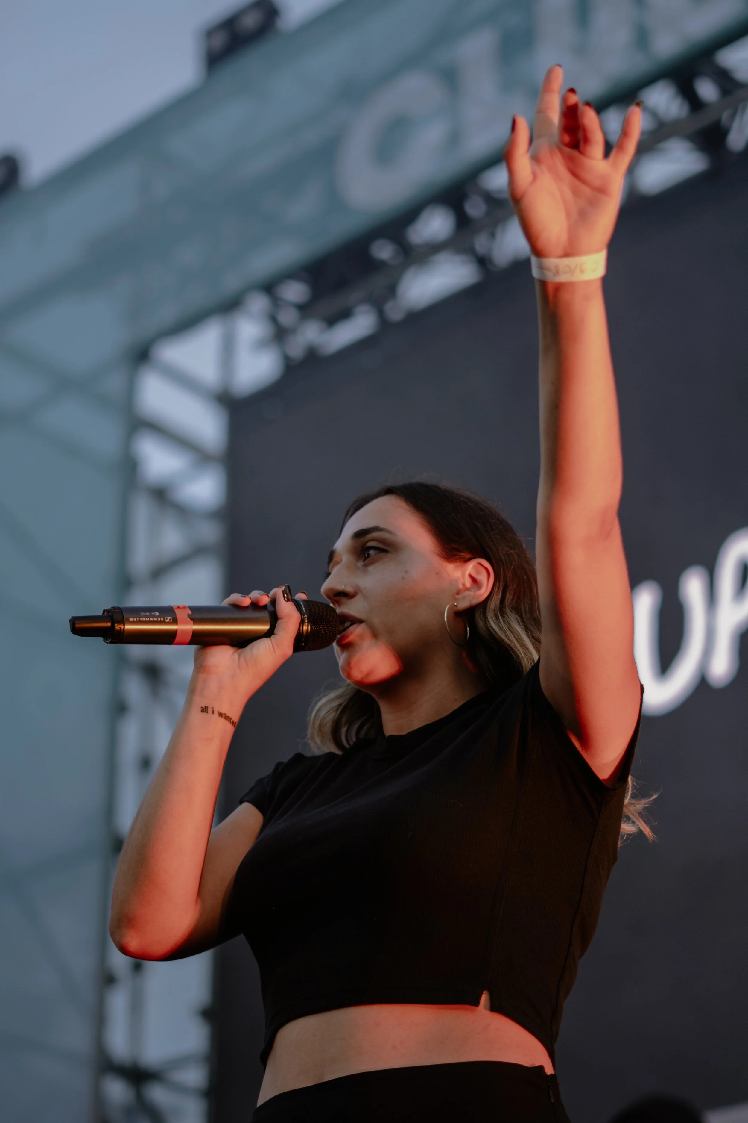 Une femme chante en haut d'une scène lors d'un concert, tenant un micro et levant la main droite.