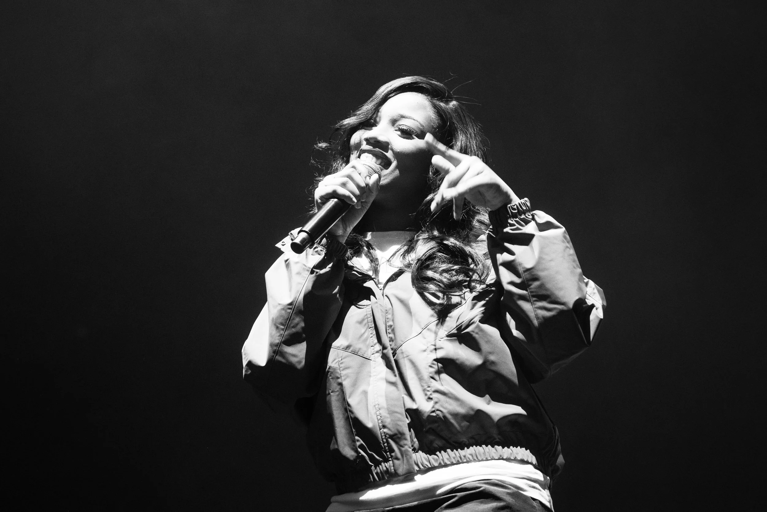 Une femme qui chante ou parle dans un microphone lors d'une performance, en noir et blanc.