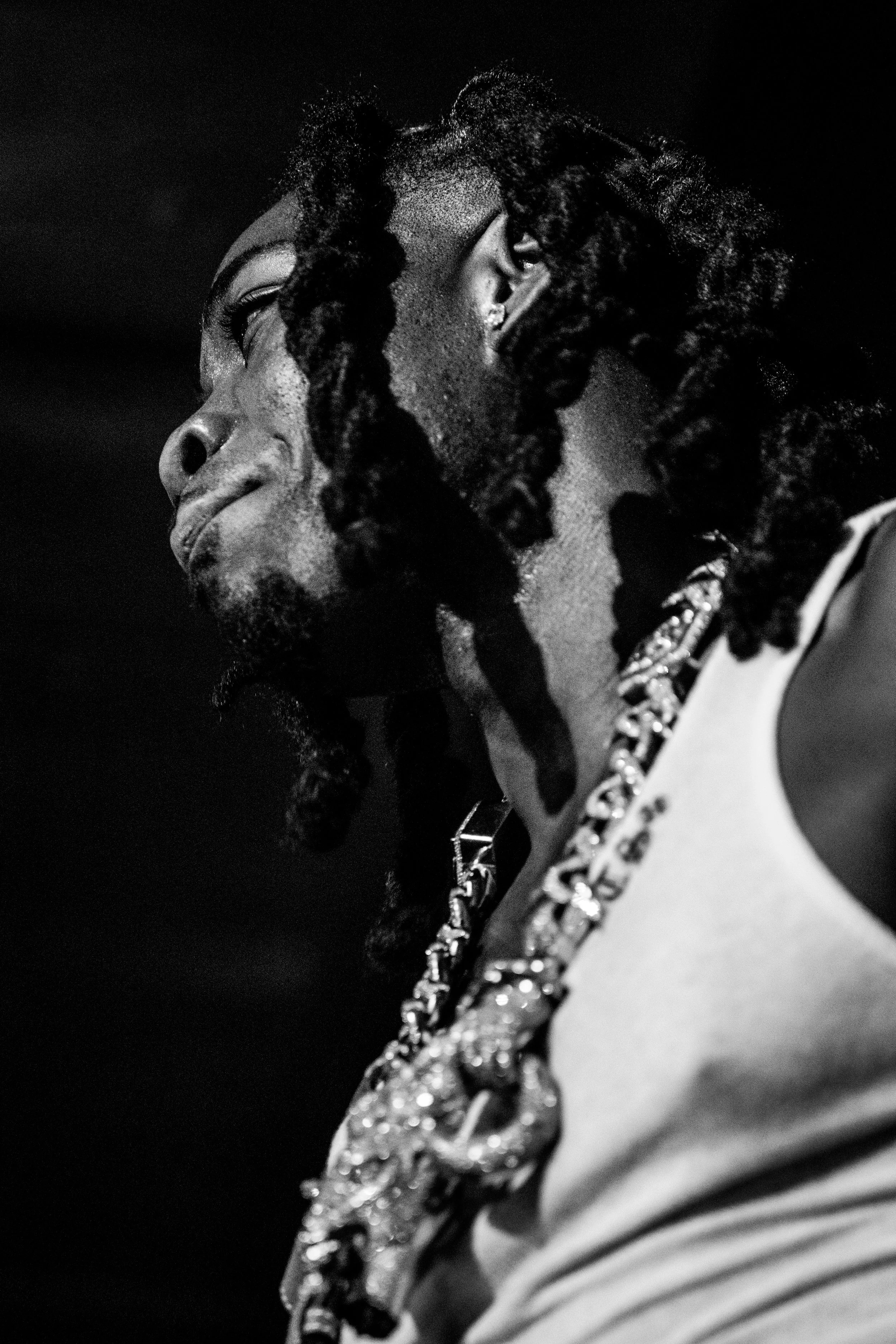 Portrait en noir et blanc d'un homme avec des cheveux torsadés portant un t-shirt sans manches et une chaîne en or.