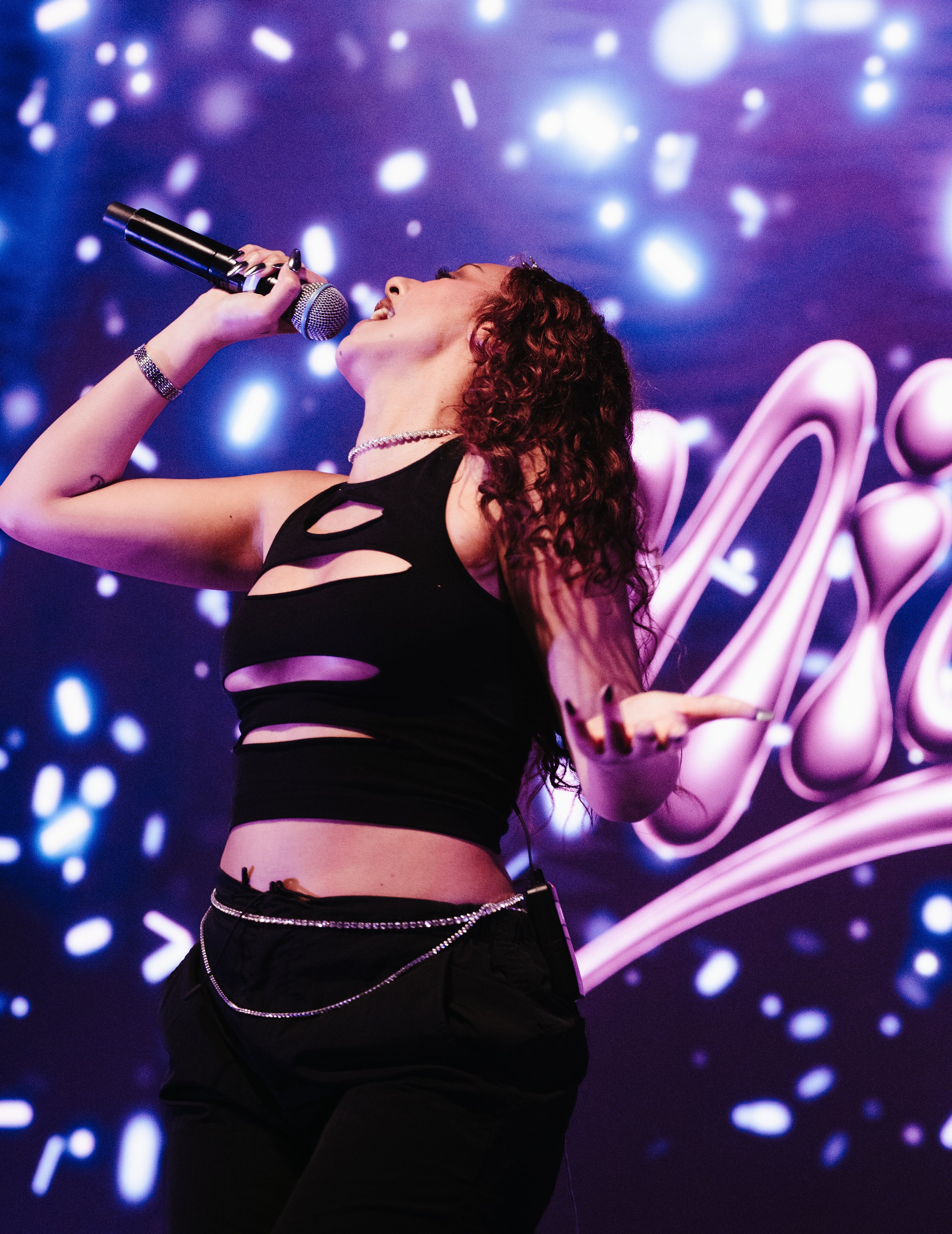 Jeune femme chantant avec un microphone lors d'une performance, fond lumineux avec des motifs abstraits en néon