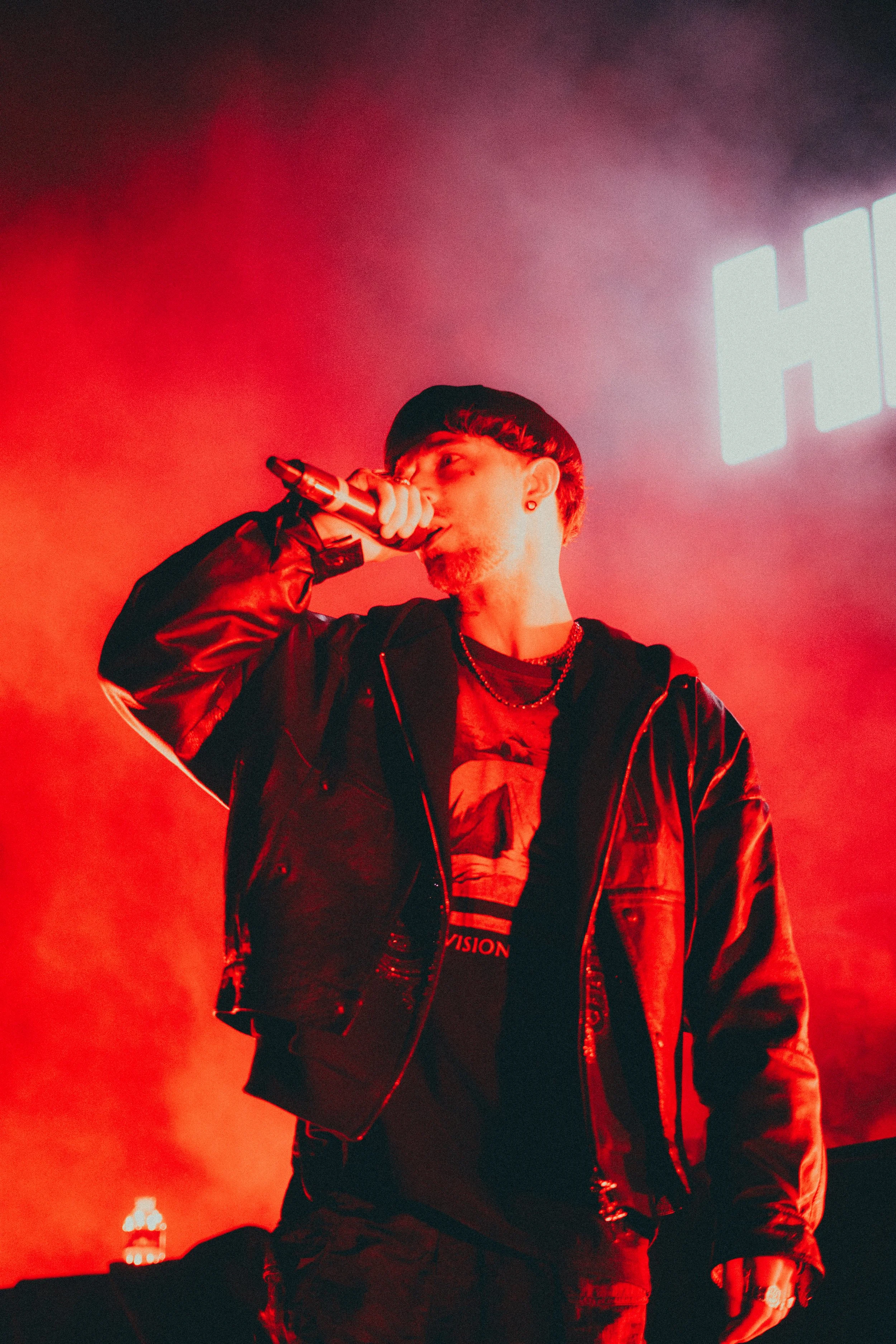 Un jeune homme chantant avec un microphone lors d'une performance sur scène, avec un éclairage rouge vif et un fond flou.