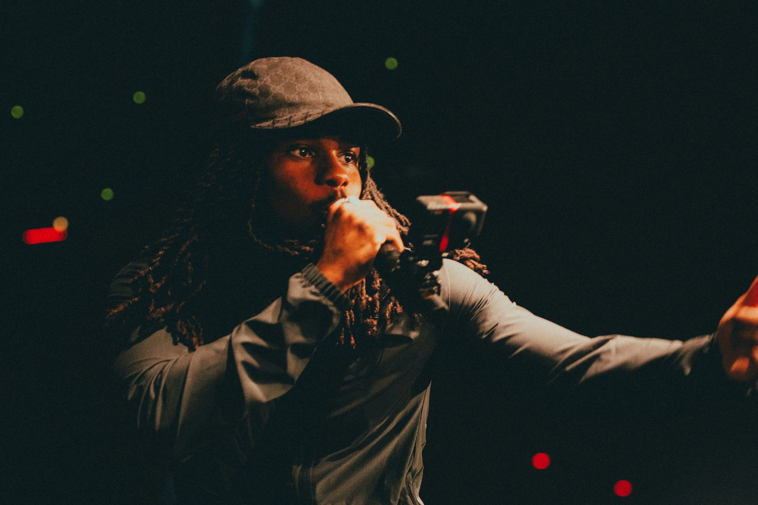 Une personne portant un chapeau, tenant un microphone, dans un environnement sombre.