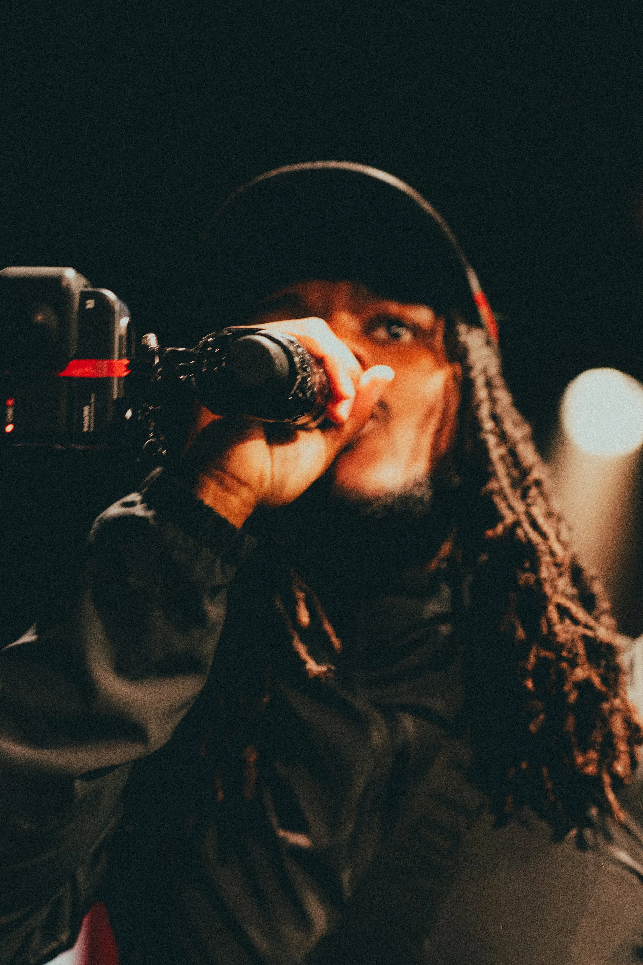 Homme avec dreadlocks portant un casque, tenant un microphone, dans un environnement sombre.