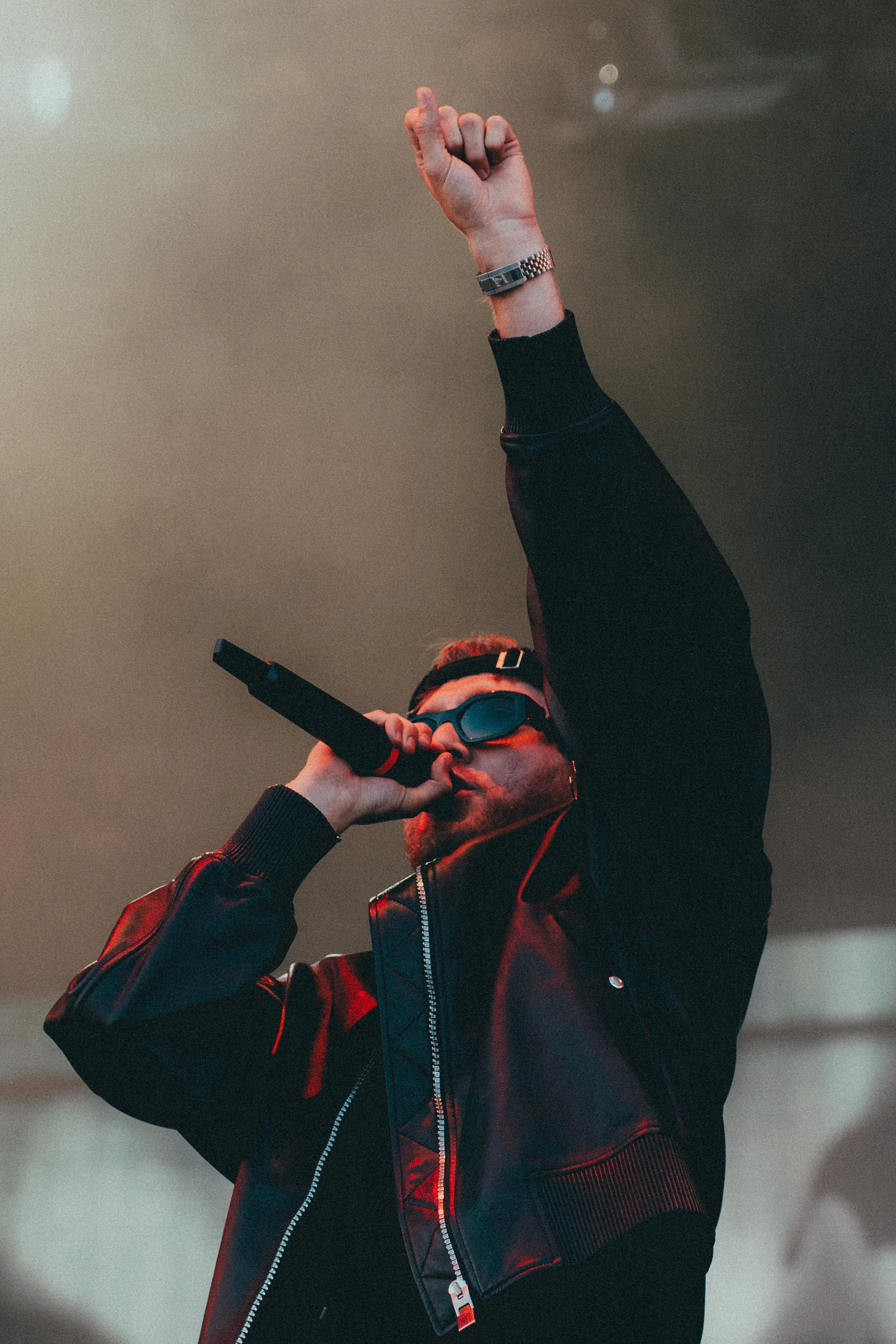 Un homme portant des lunettes de soleil, un blouson noir en cuir, chantant dans un microphone lors d'une performance.