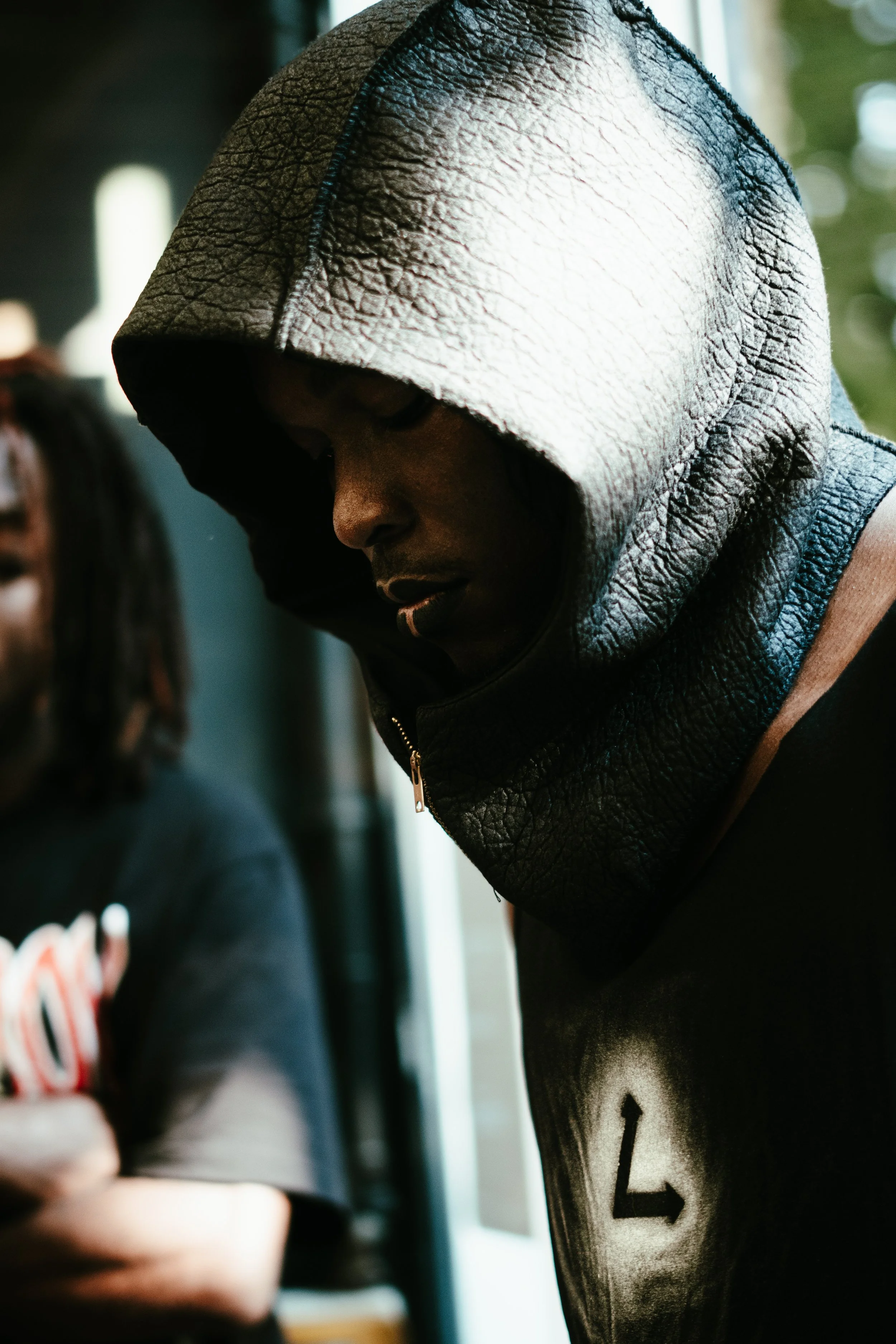 Un jeune homme portant une veste en cuir et un bonnet à capuche en train de regarder son téléphone, dans un intérieur avec lumière naturelle