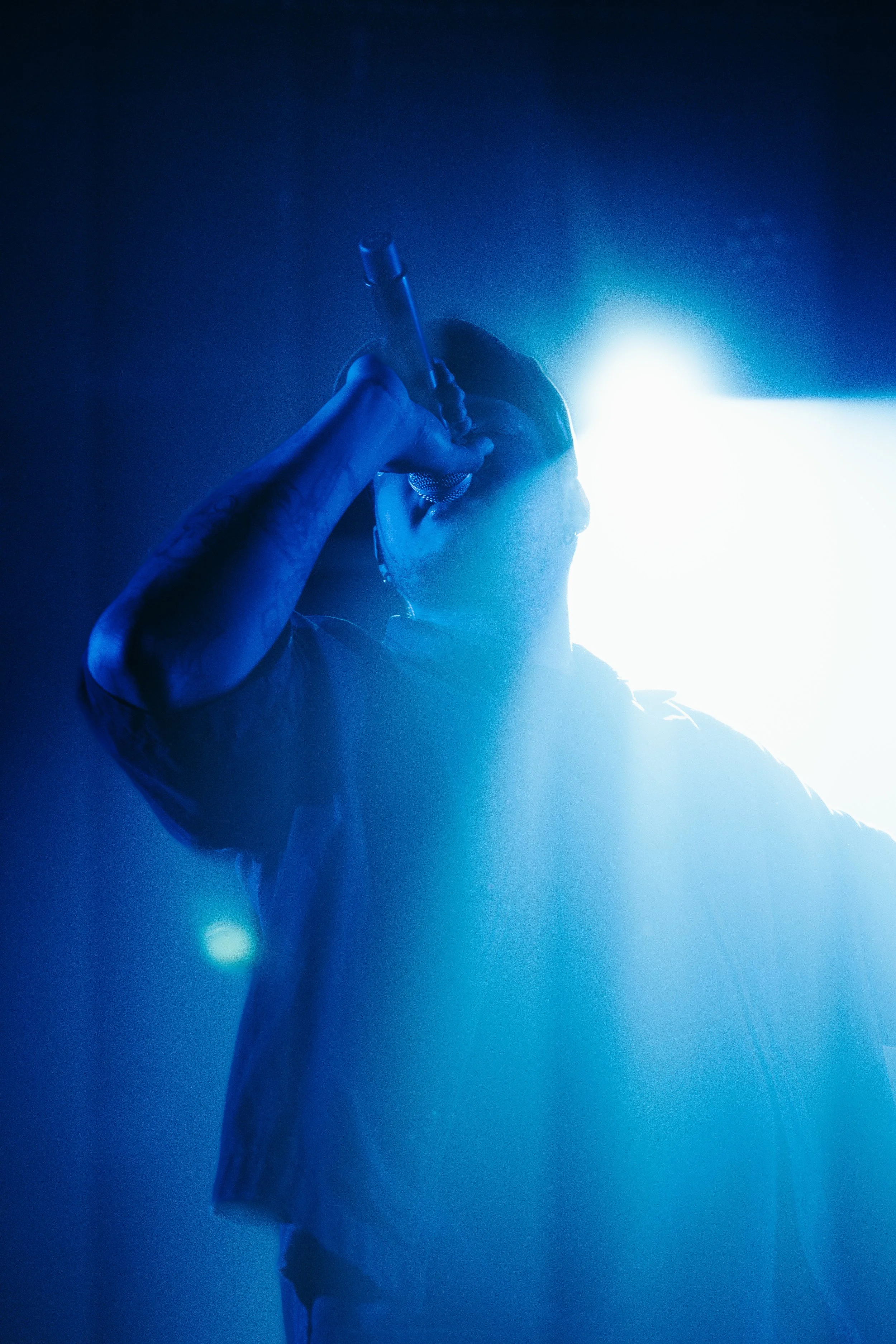 Un artiste de spectacle chante avec un micro dans un éclairage bleuté.