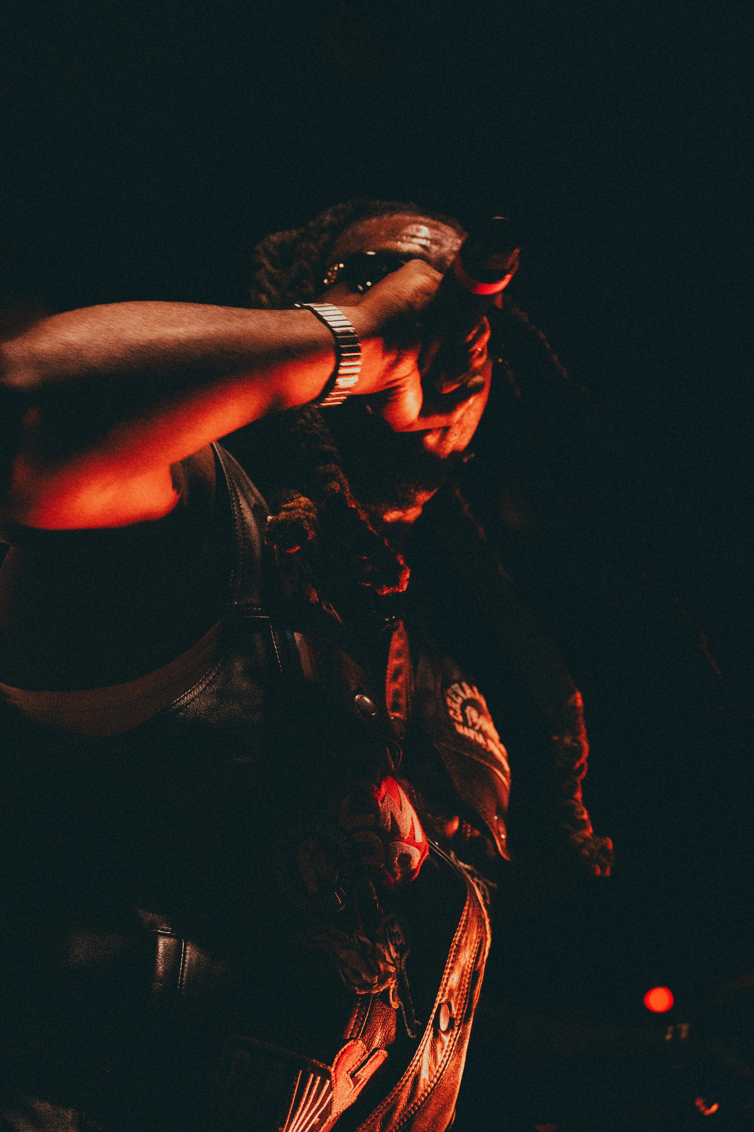 Un homme portant une veste en cuir noir, tenant un microphone, dans une ambiance sombre avec un éclairage rouge.