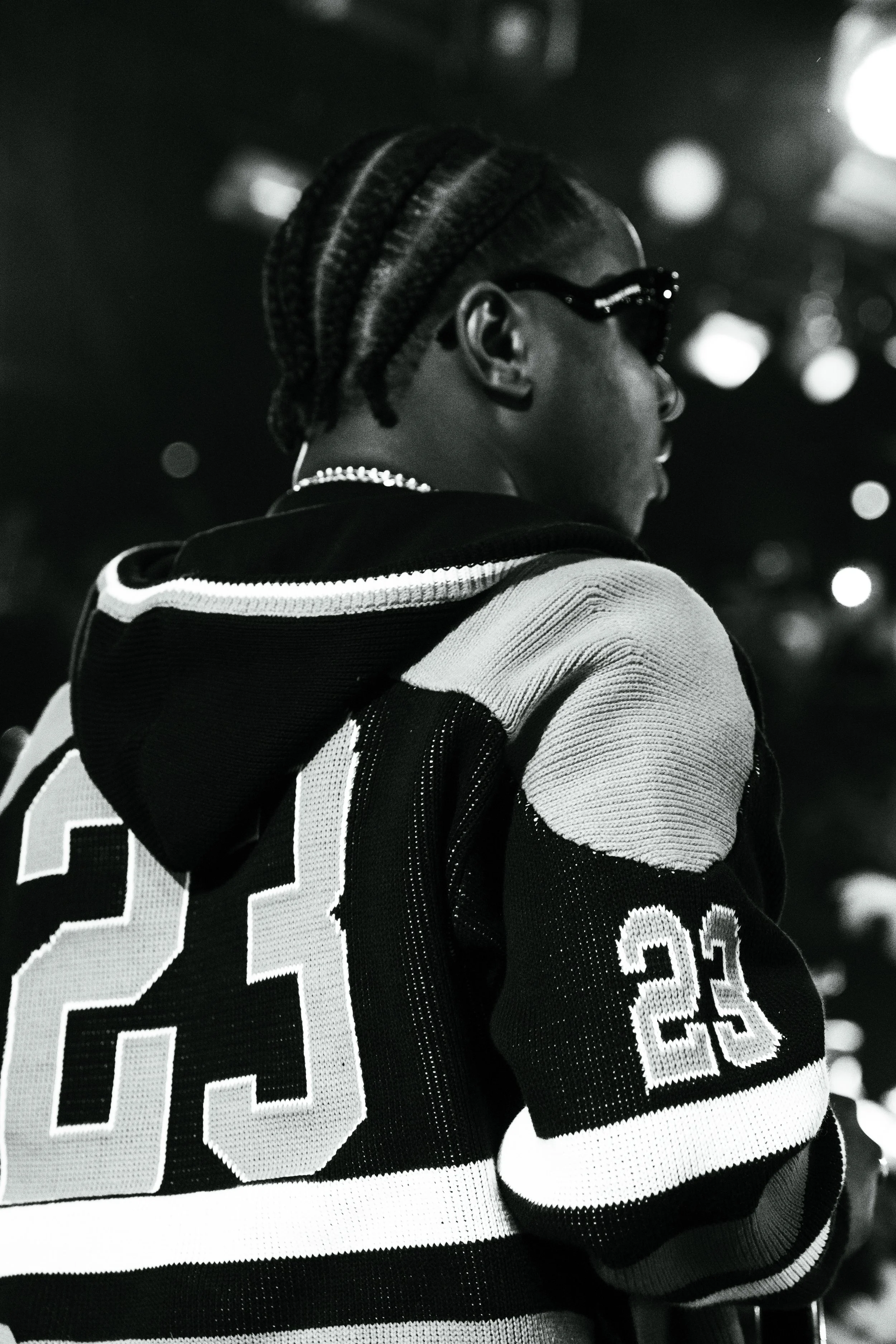 Portrait d'une personne portant des lunettes de soleil et une veste à rayures avec le numéro 23, en noir et blanc.