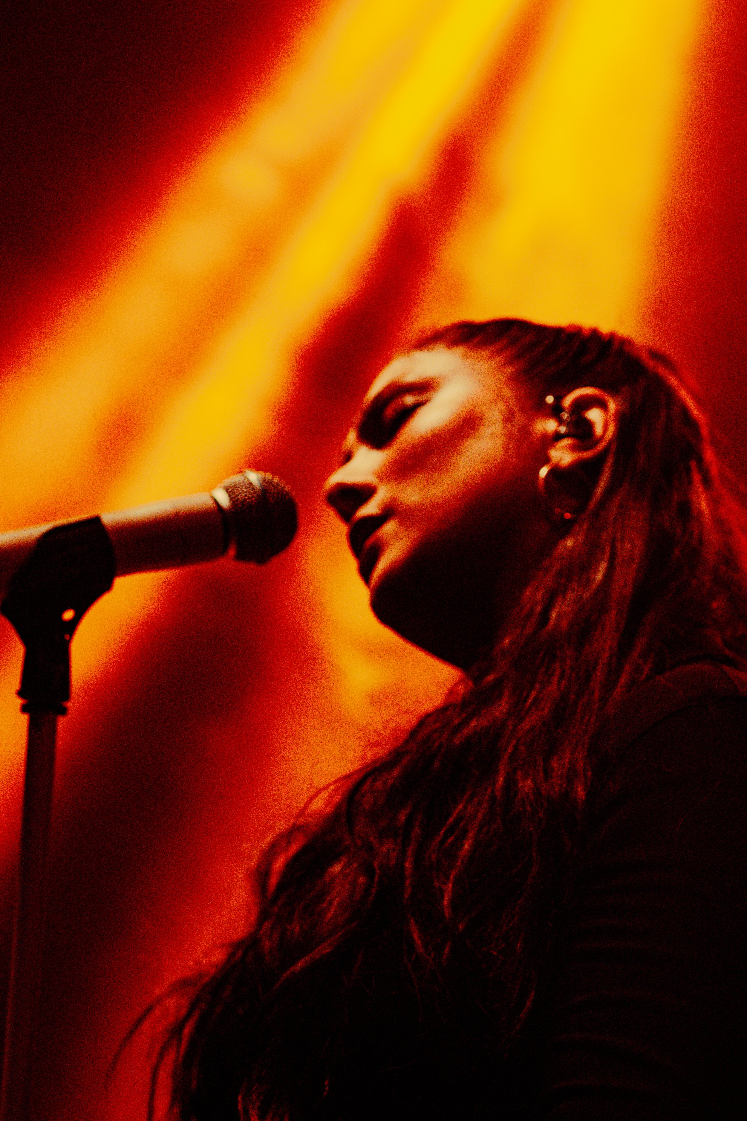 Une femme avec des cheveux longs chantant ou parlant dans un microphone, éclairée par des projecteurs jaunes et rouges.