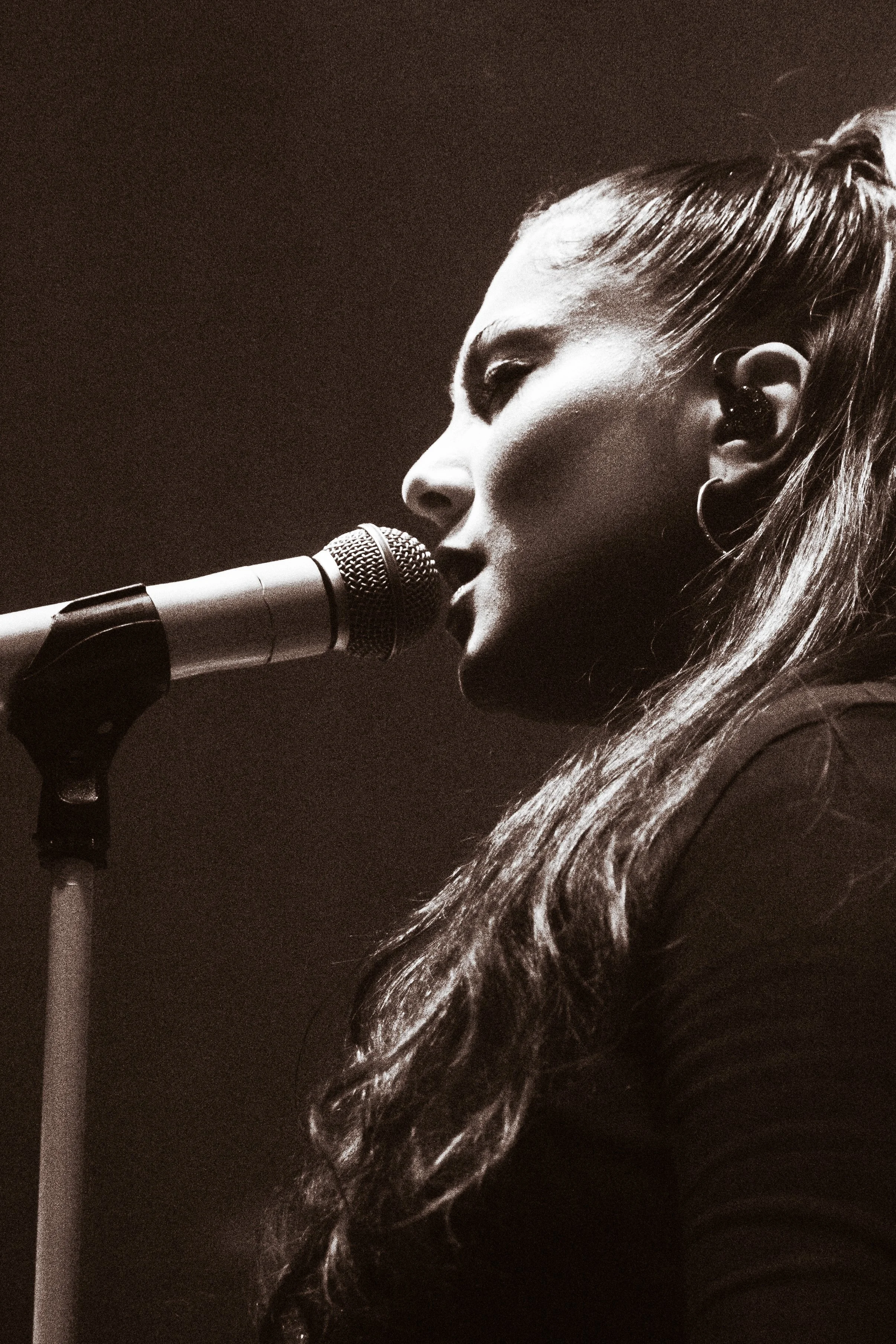 Une femme chante dans un micro, avec des cheveux longs et une attitude expressive, en noir et blanc.