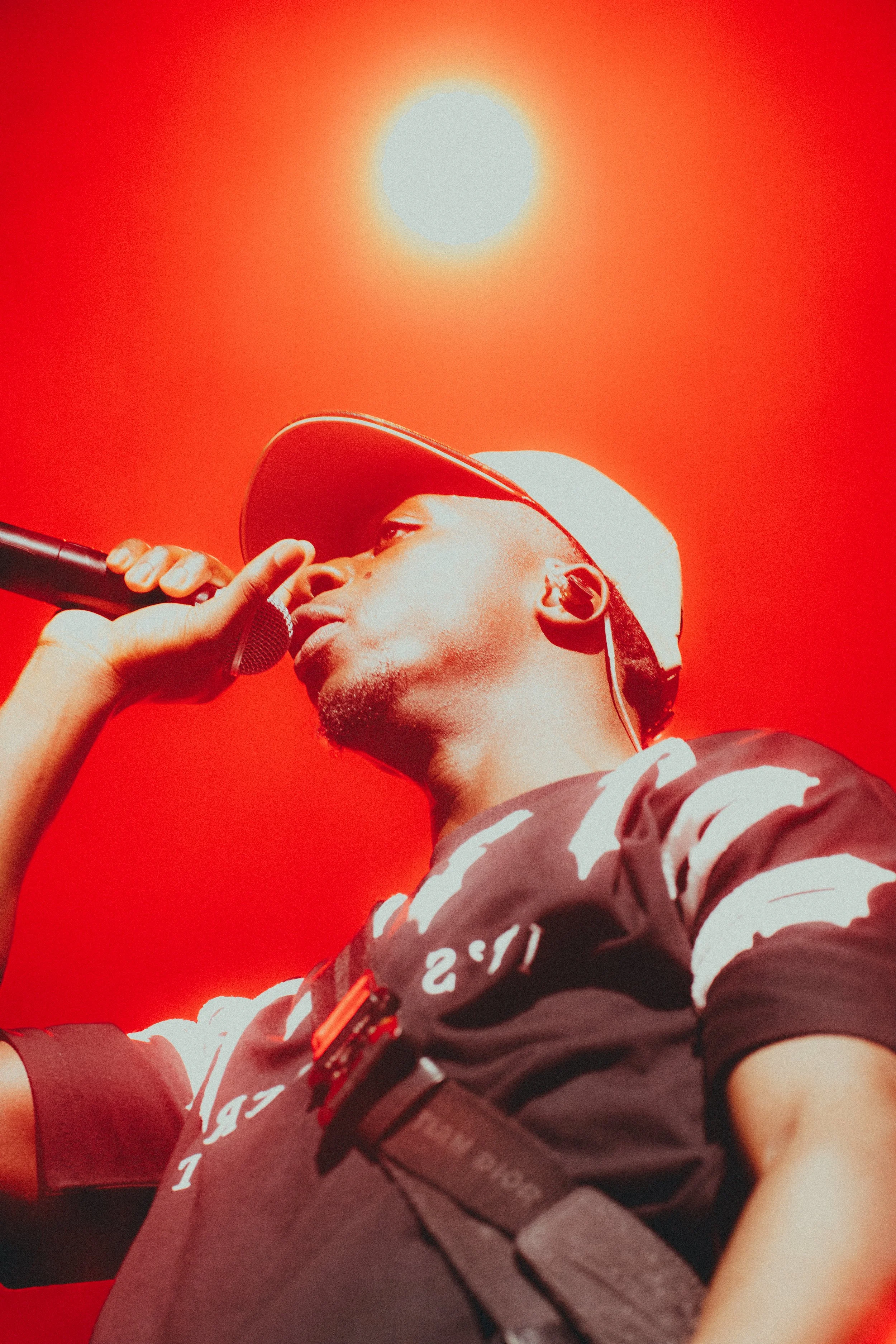 Jeune homme de profil portant un casque blanc et un t-shirt noir et blanc, tenant un microphone, avec un ciel rouge en arrière-plan