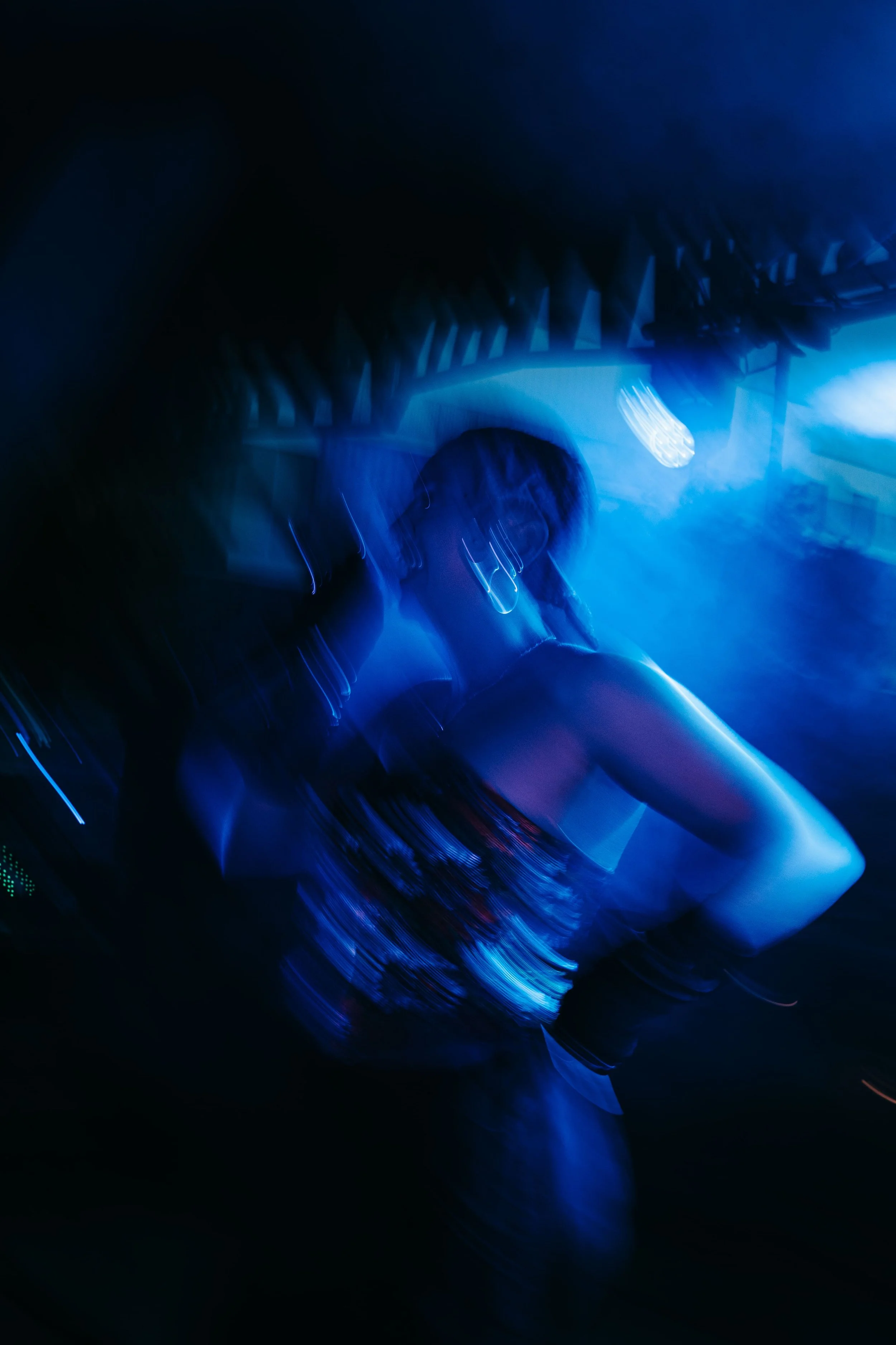 Une femme dans une discothèque sous des lumières bleues, portant un haut à motifs et des boucles d'oreilles.