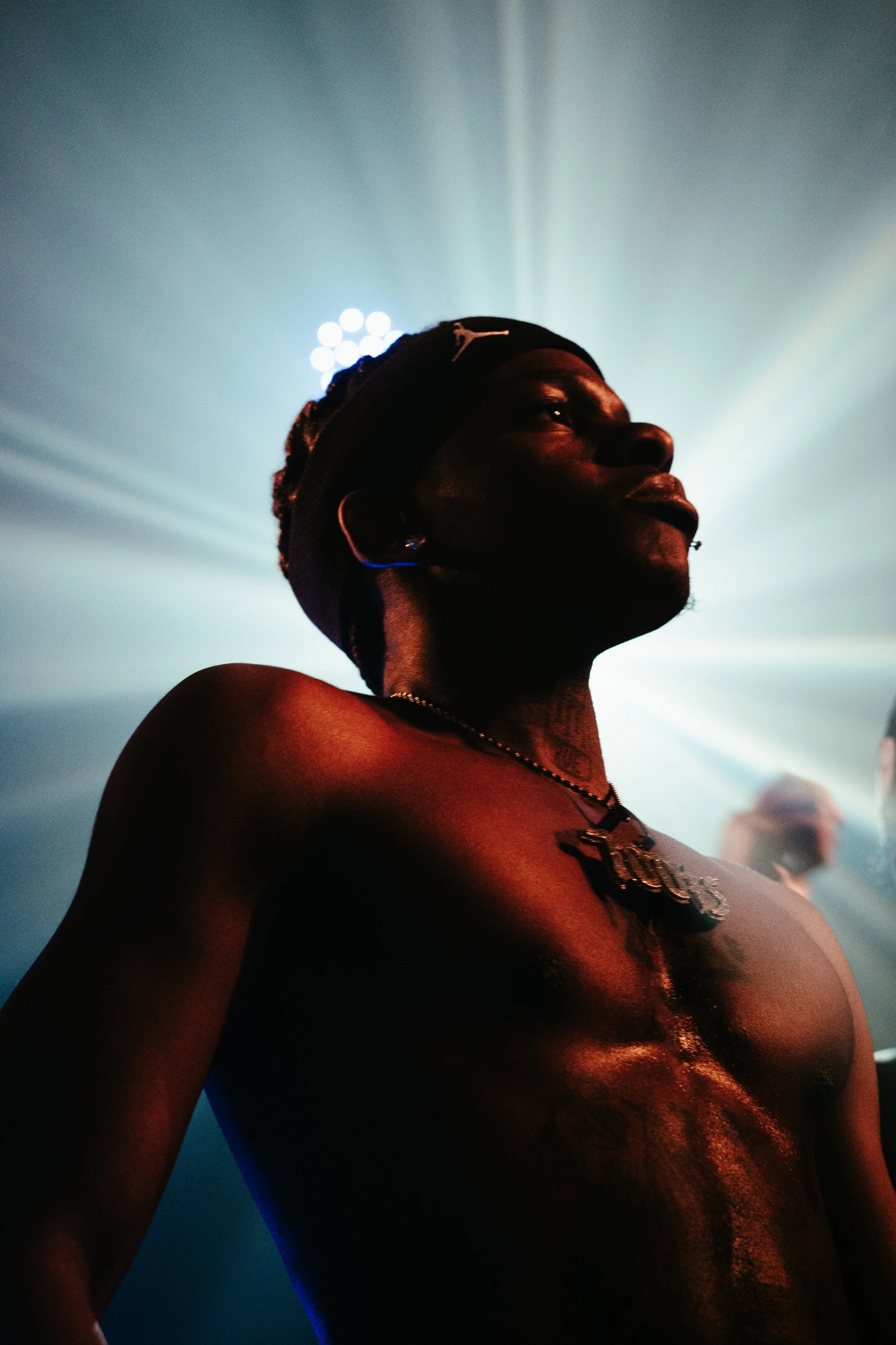 Une personne nue portant des bijoux, avec une arrière-plan de lumières de scène, créée une silhouette mystérieuse et expressive.