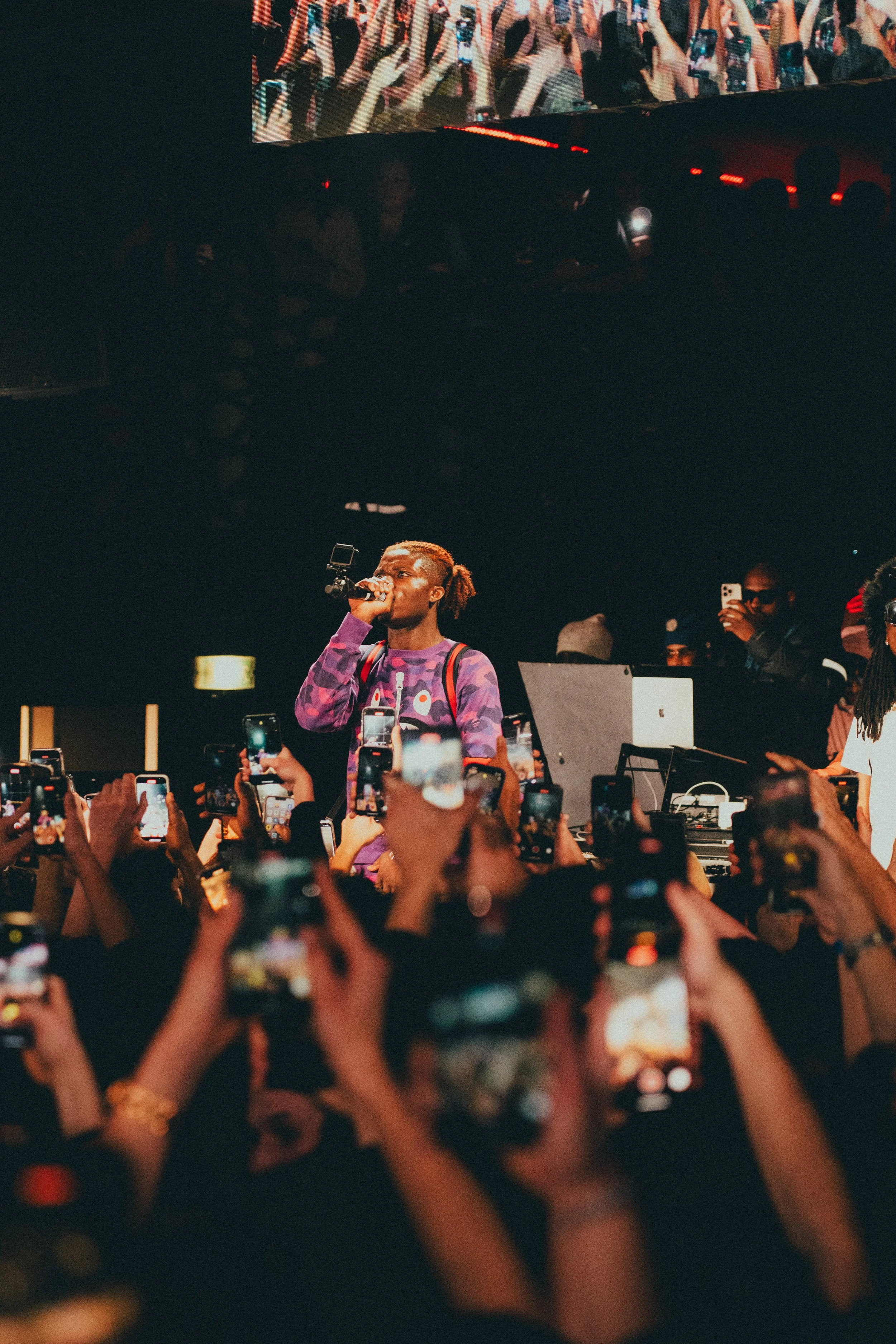 Un artiste chante lors d'un concert entouré d'une foule prenant des photos avec leurs téléphones portables.