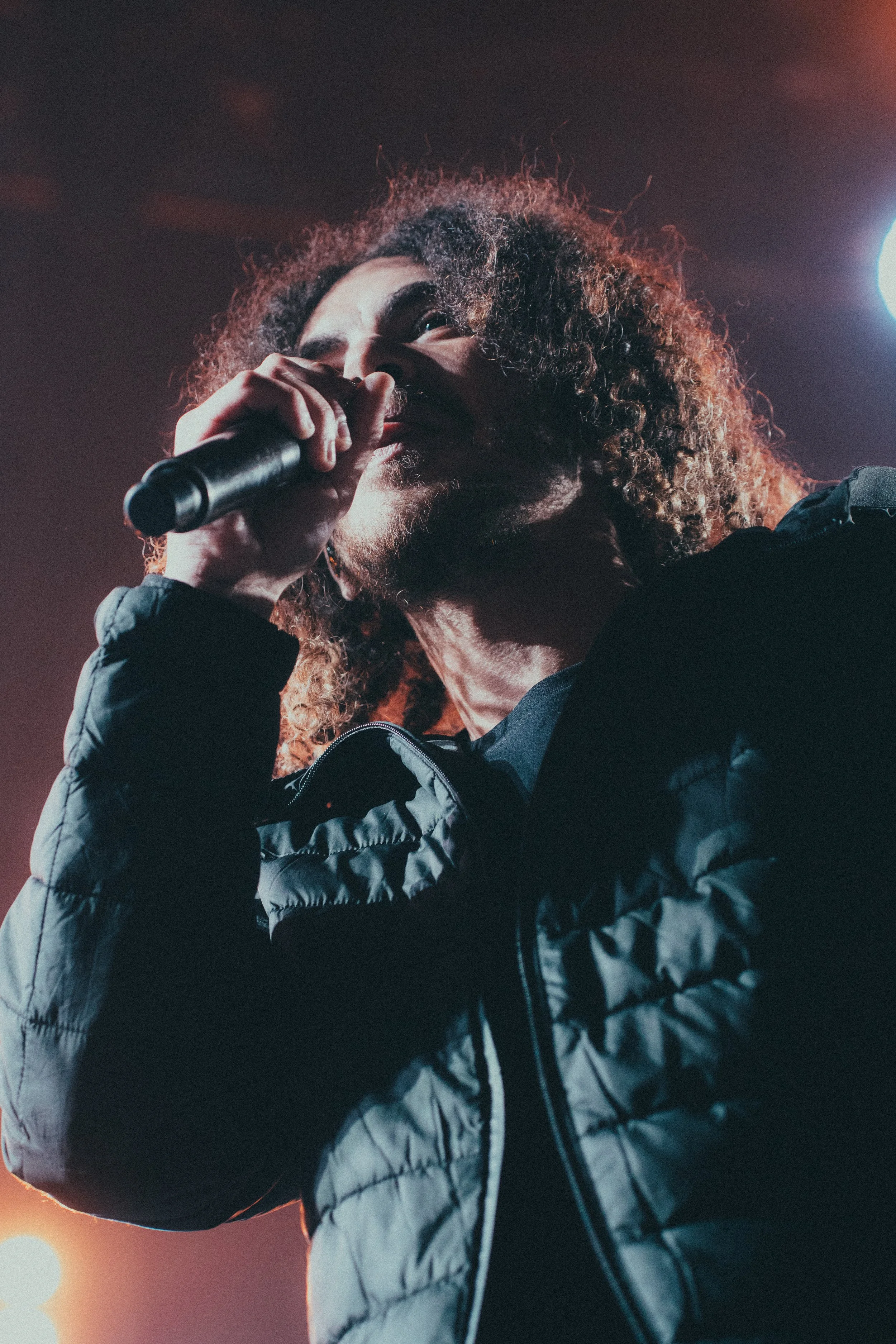 Un homme avec des cheveux bouclés bruns filme avec un micro lors d'un concert.