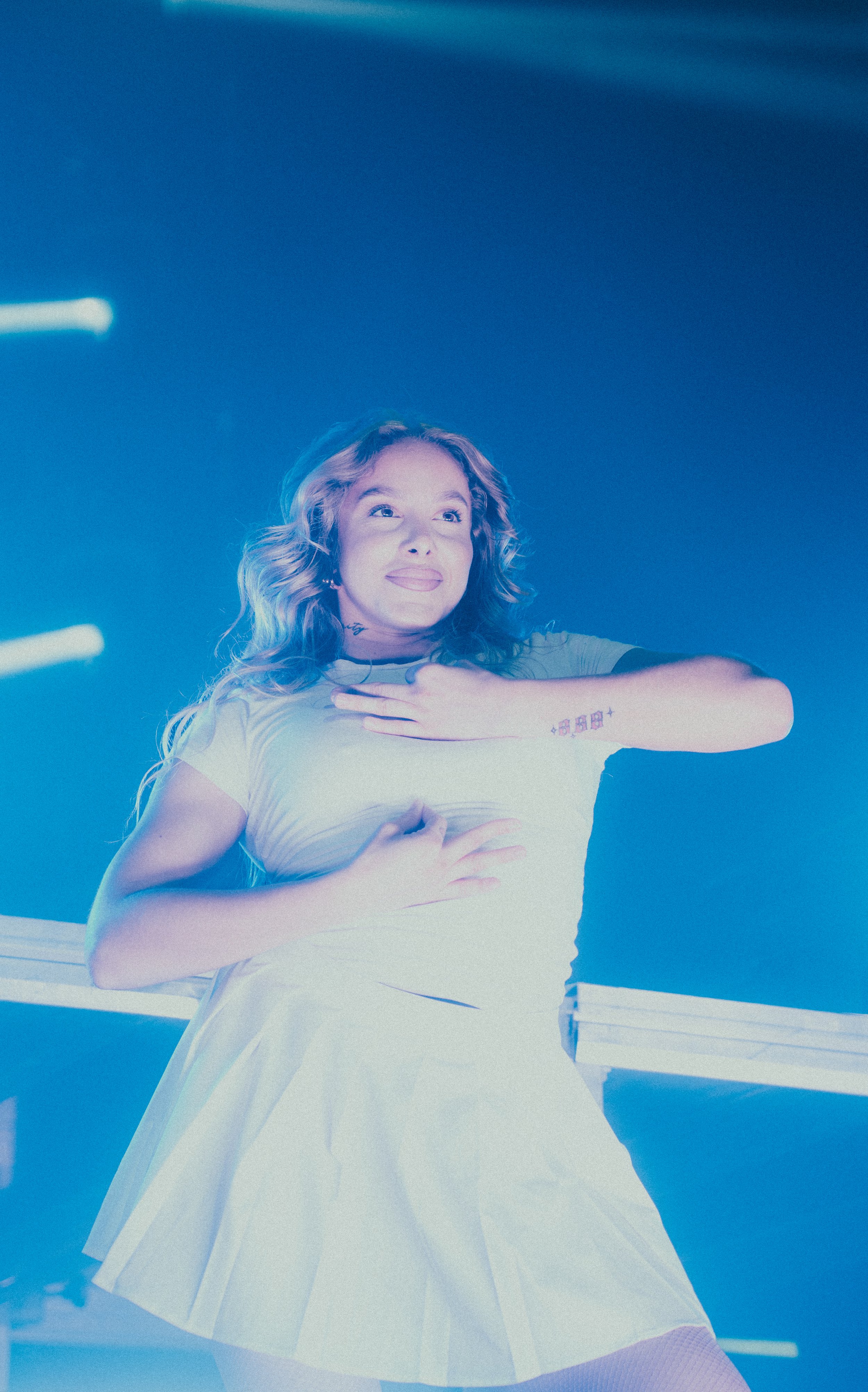 Une jeune femme souriante danse dans un luminisme bleu avec une robe blanche, dans un environnement de scène ou de concert.