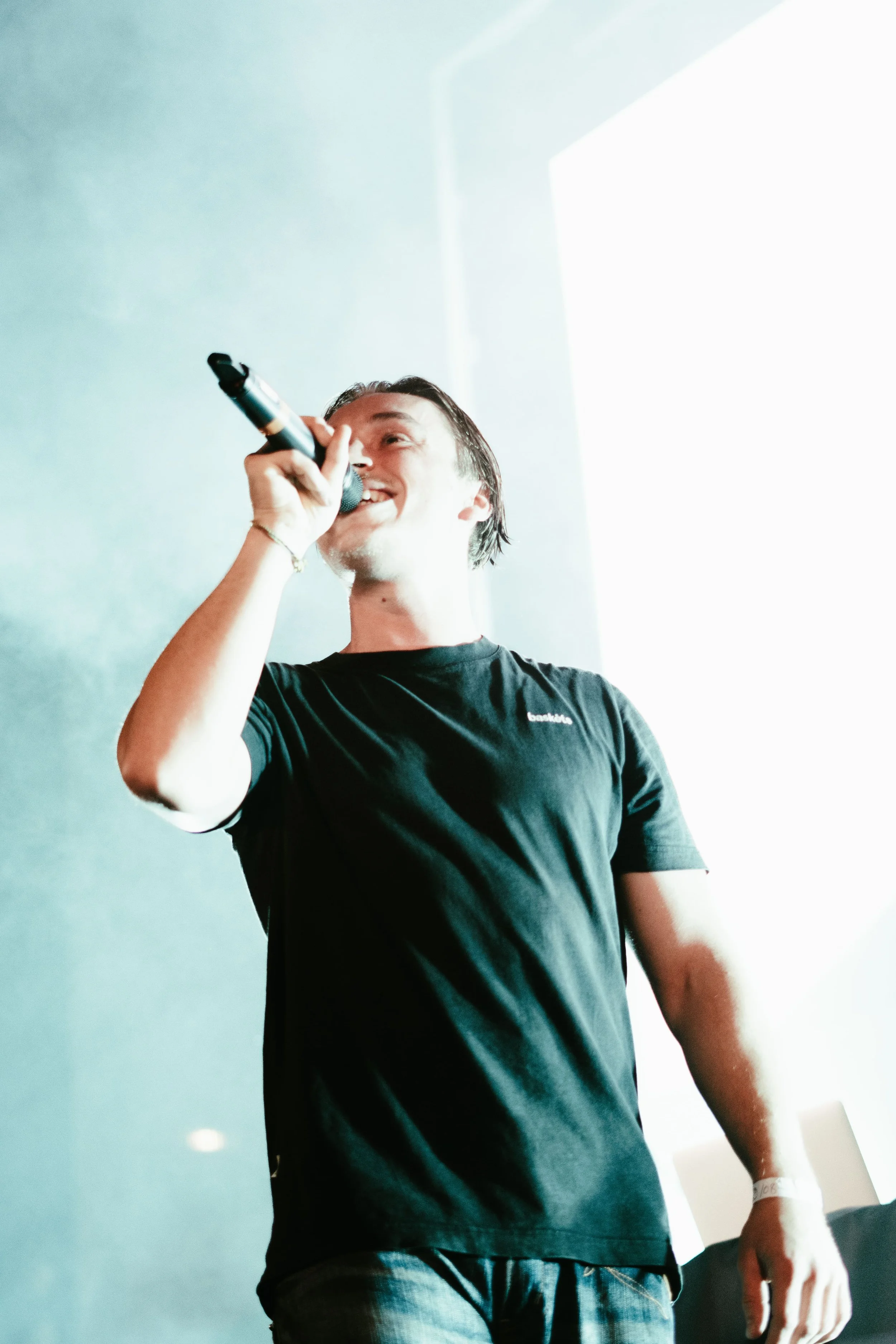 Un jeune homme chante ou parle en tenant un micro dans une pièce lumineuse.