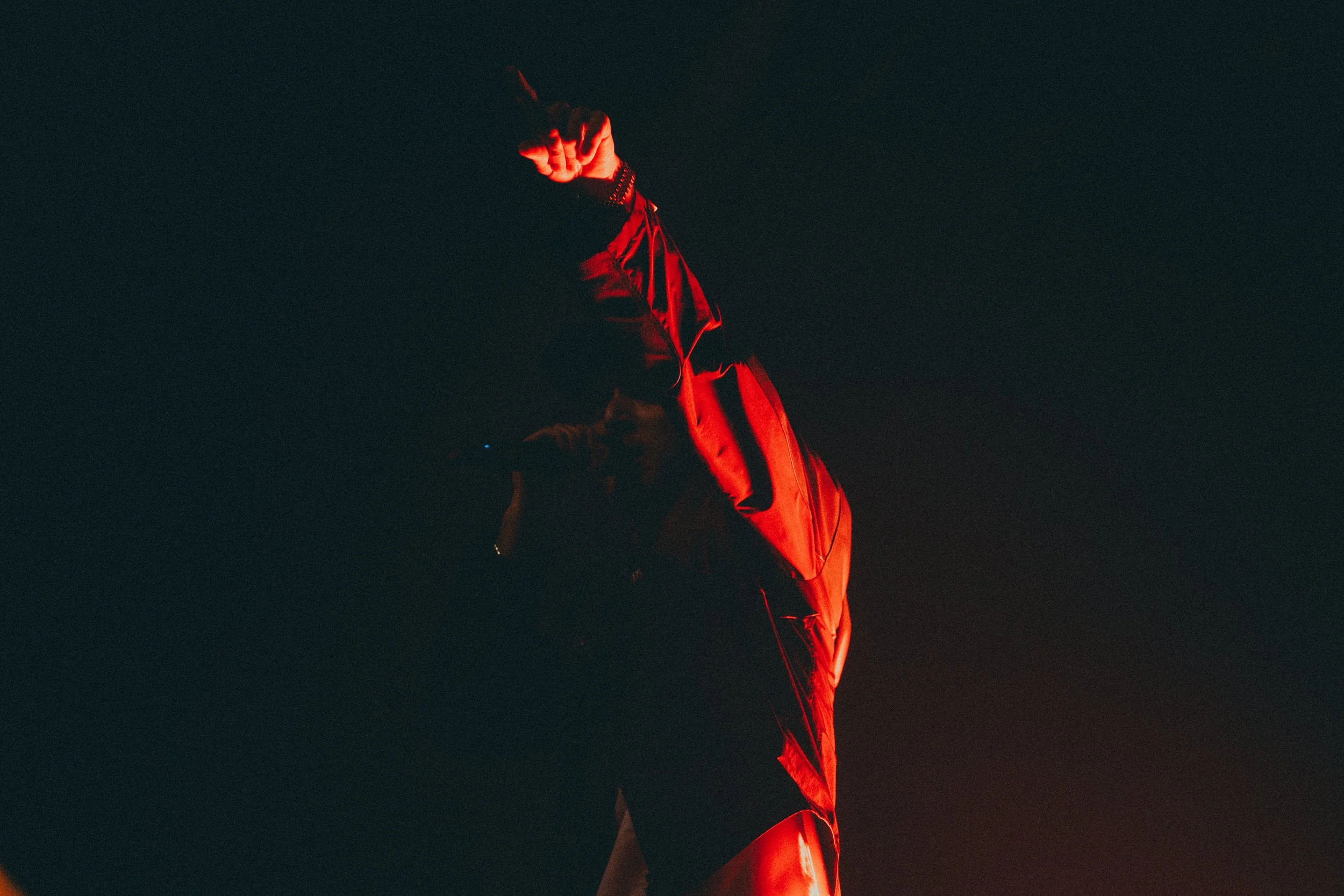 Une personne portant un costume noir, éclairée par un éclairage rouge dans l'obscurité.