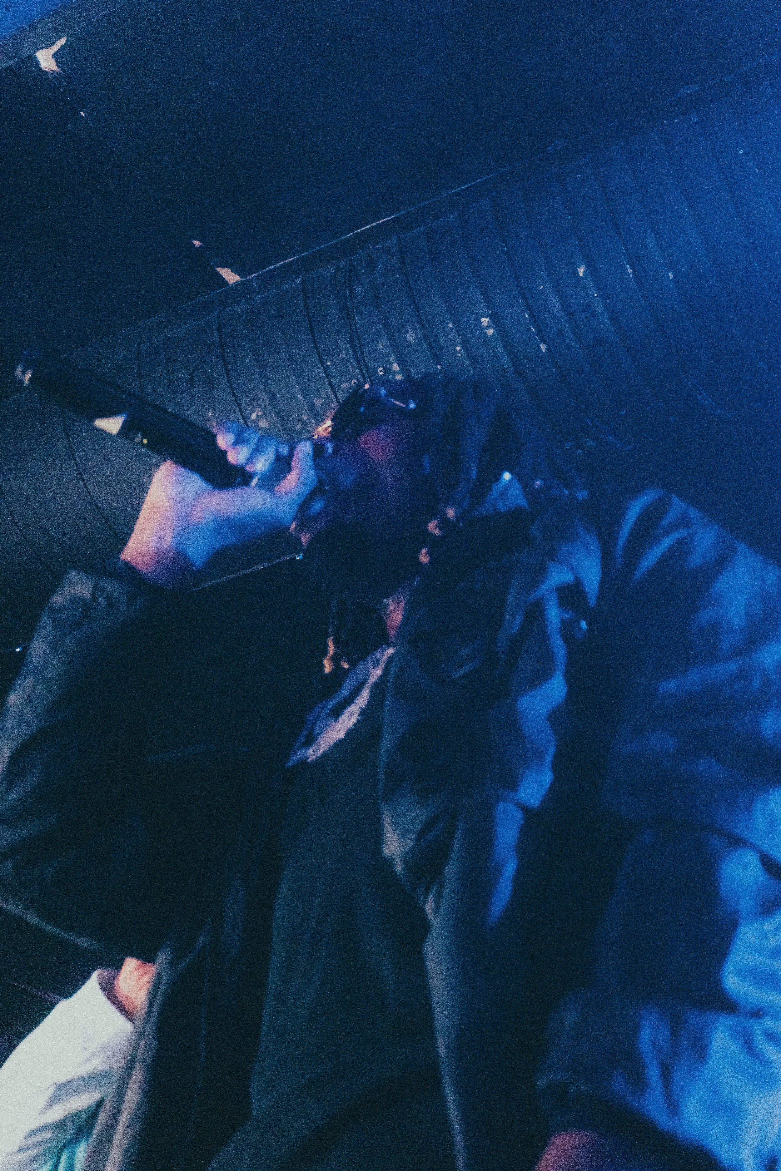 Personne portant une veste noire, tenant un instrument à vent, avec un fond sombre et luminescent.