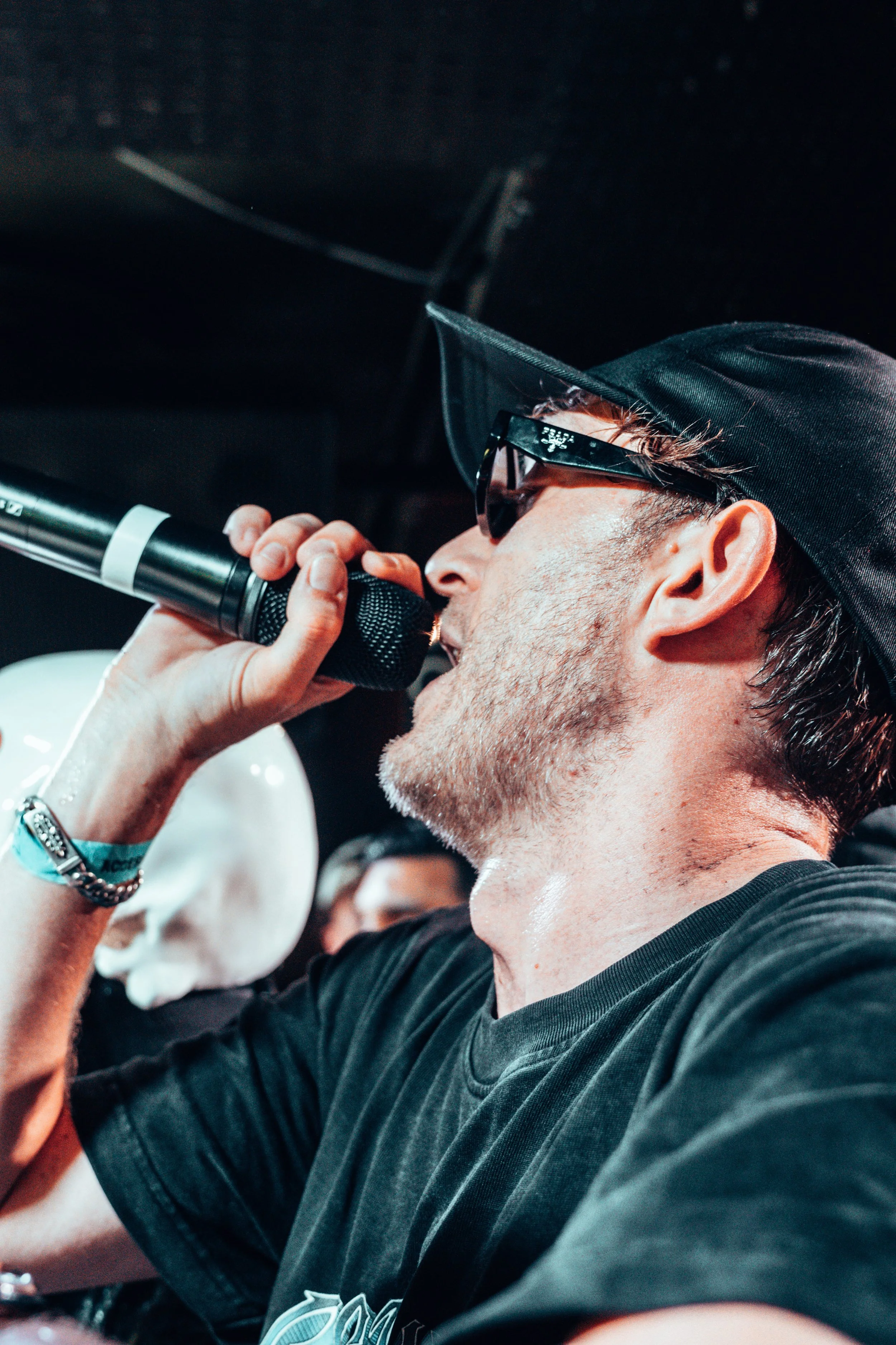 Un homme portant une casquette noire et des lunettes de soleil chante dans un microphone lors d'une performance.