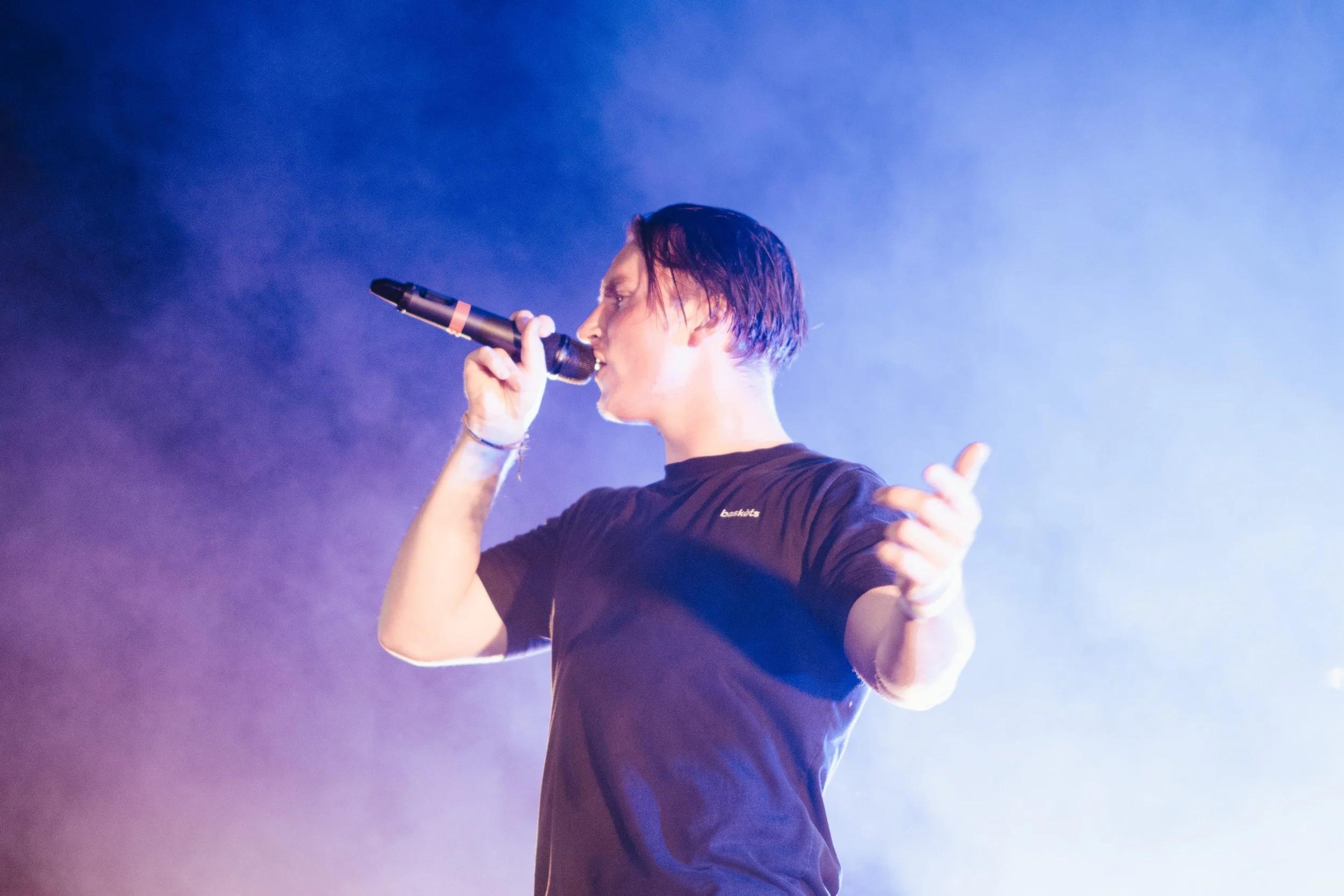 Jeune homme chantant avec micro sur scène illuminée par des lumières bleues et violettes