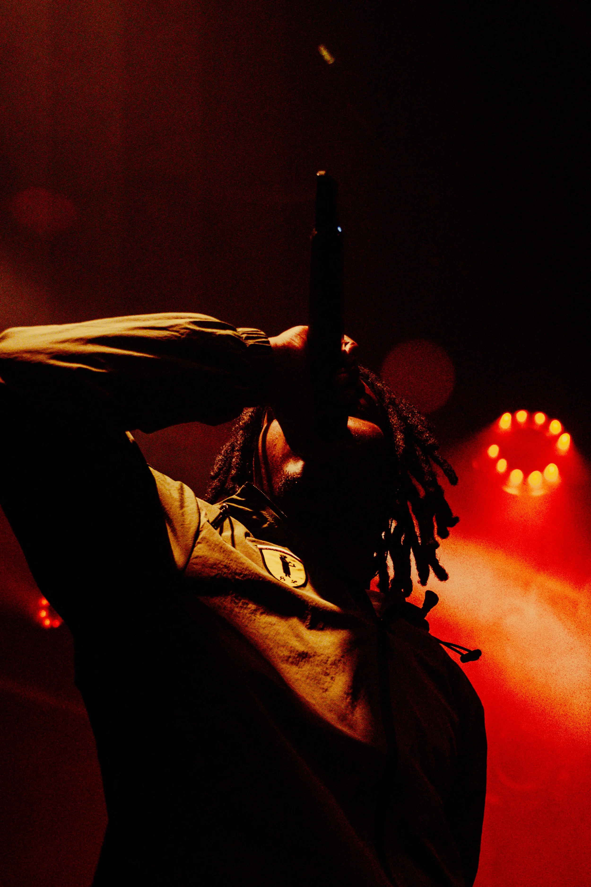 Un artiste de rap en performance en scène avec des lumières rouges en arrière-plan, tenant un micro près de la bouche