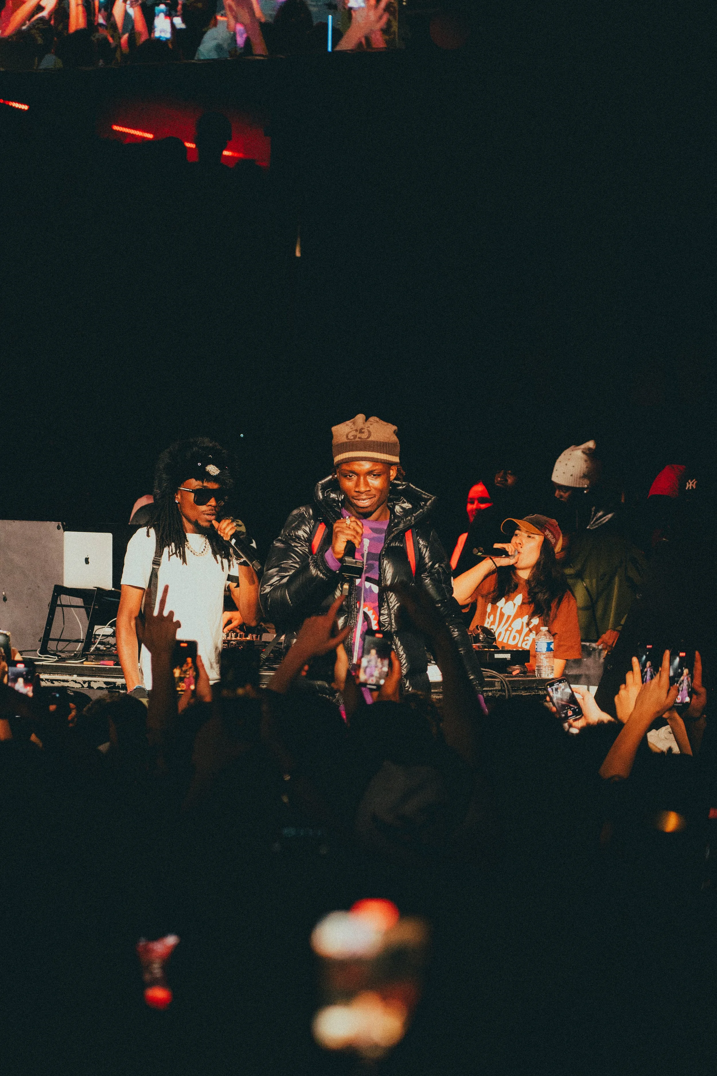 Une performance musicale en direct avec des artistes sur scène, entourés d'une foule qui prend des photos et enregistre avec leurs téléphones.