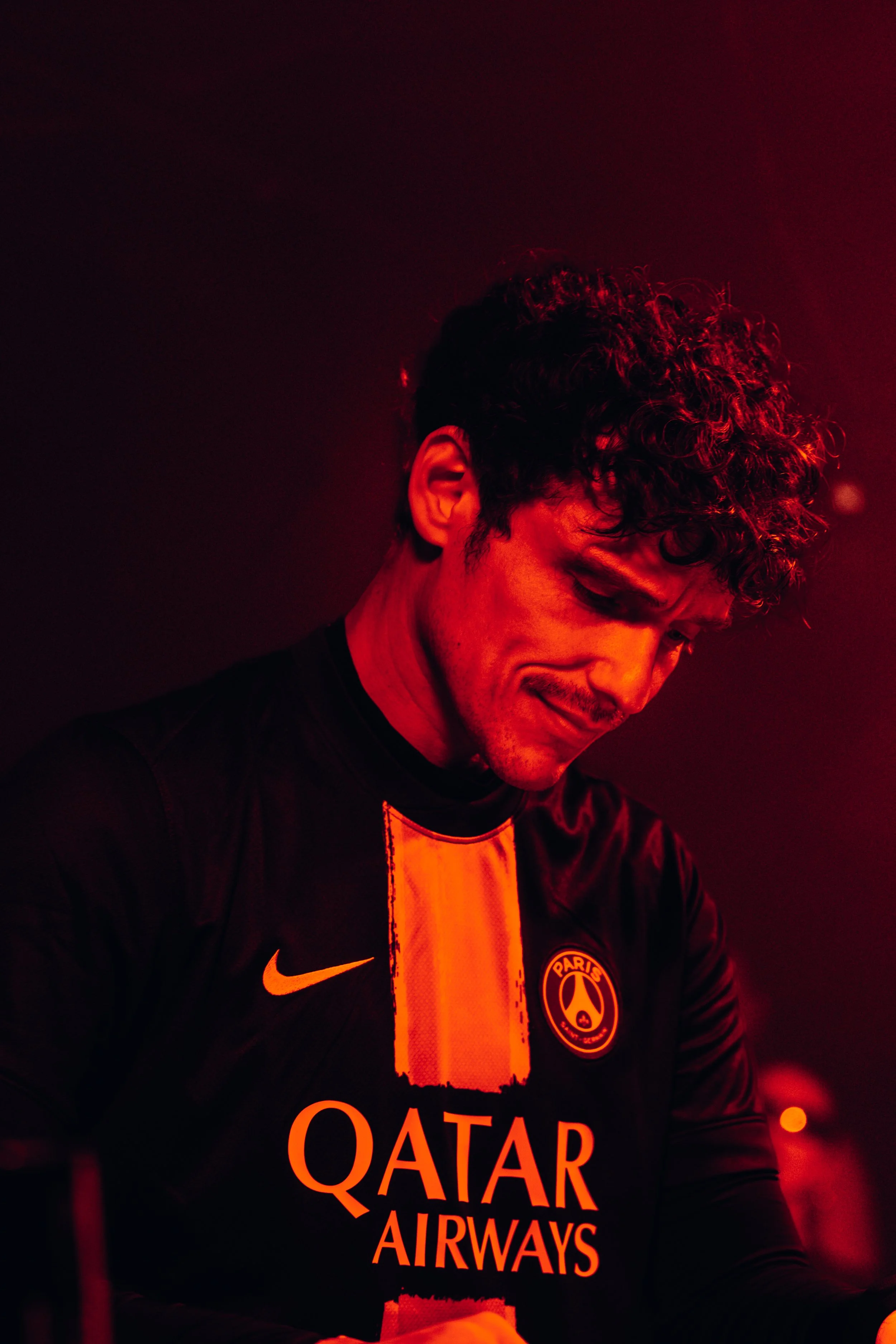 Femme en maillot de football du Paris Saint-Germain avec logo Qatar Airways, dans une scène sombre avec un éclairage rouge.