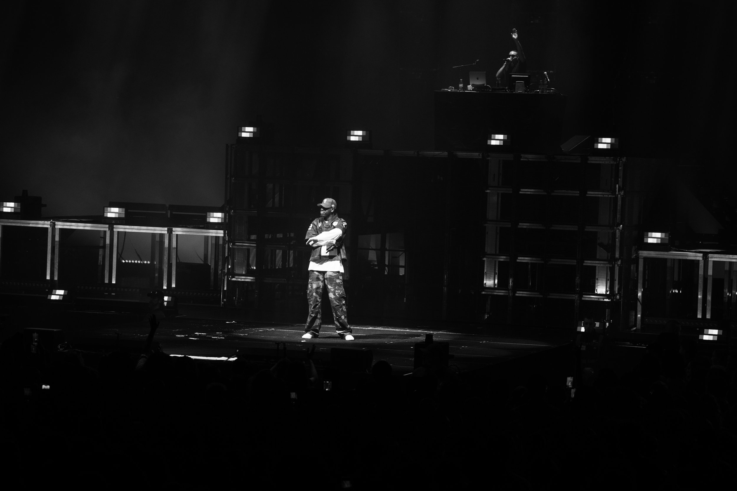 Un homme avec des vêtements décontractés, debout sur scène dans un spectacle de spectacle avec un DJ en arrière-plan.