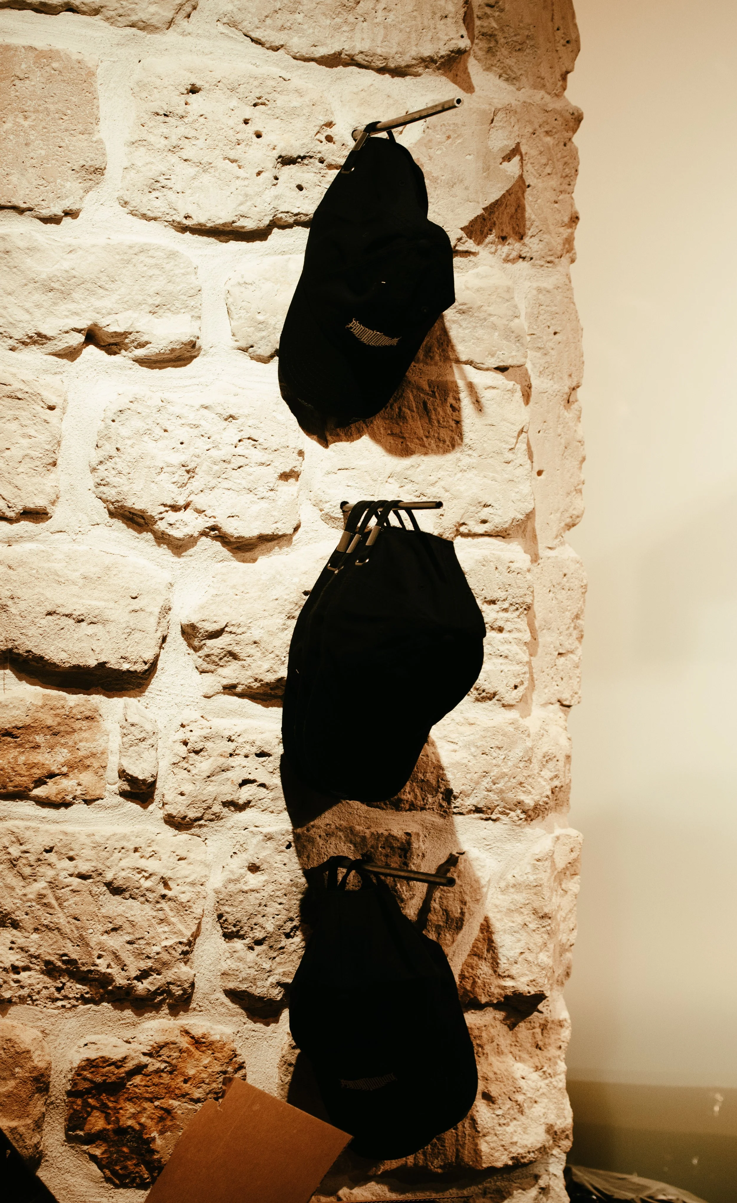 Trois casquettes noires suspendues sur un mur en pierre.