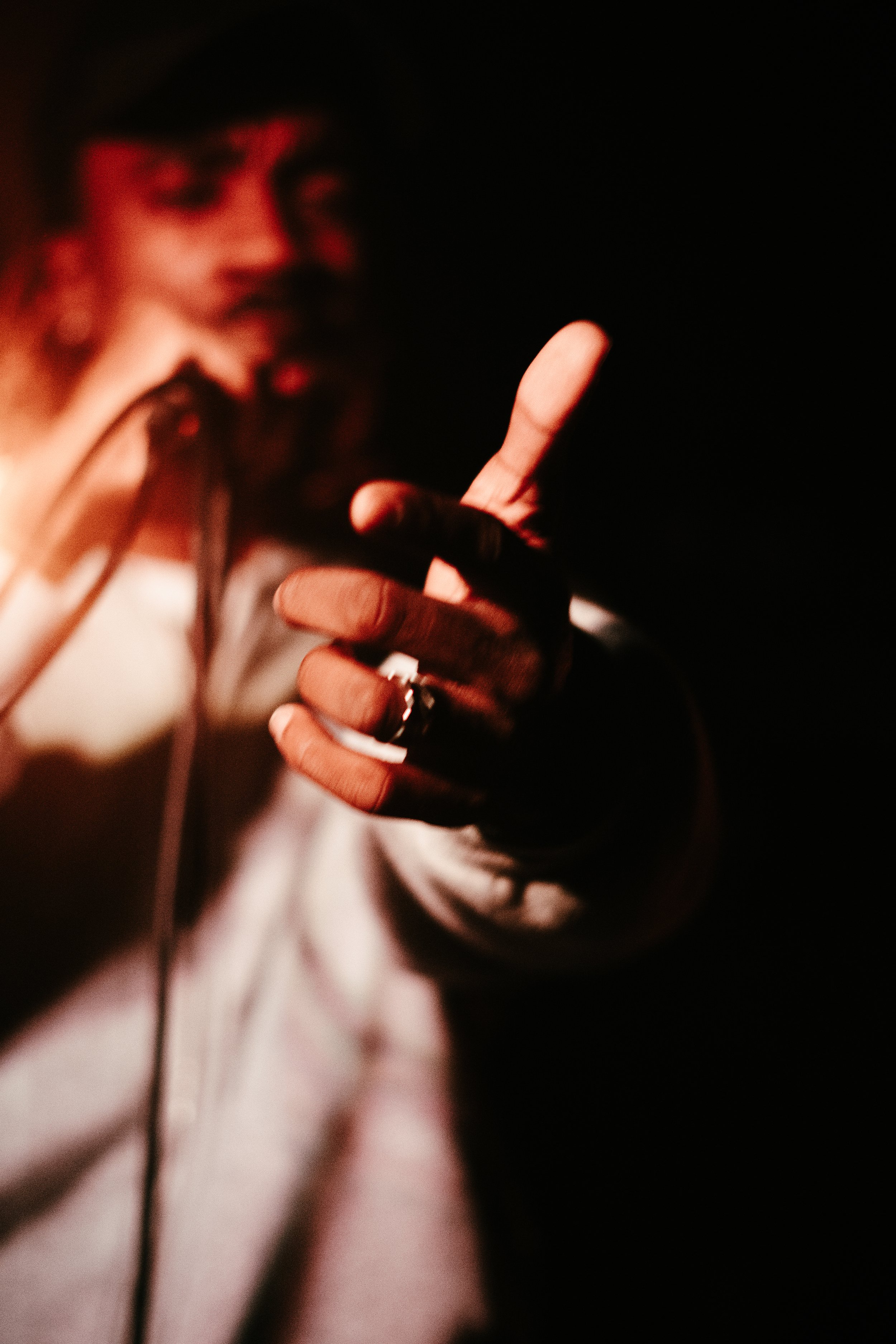 Une personne floutée faisant un geste de la main dans l'obscurité, avec un éclairage chaud sur la main