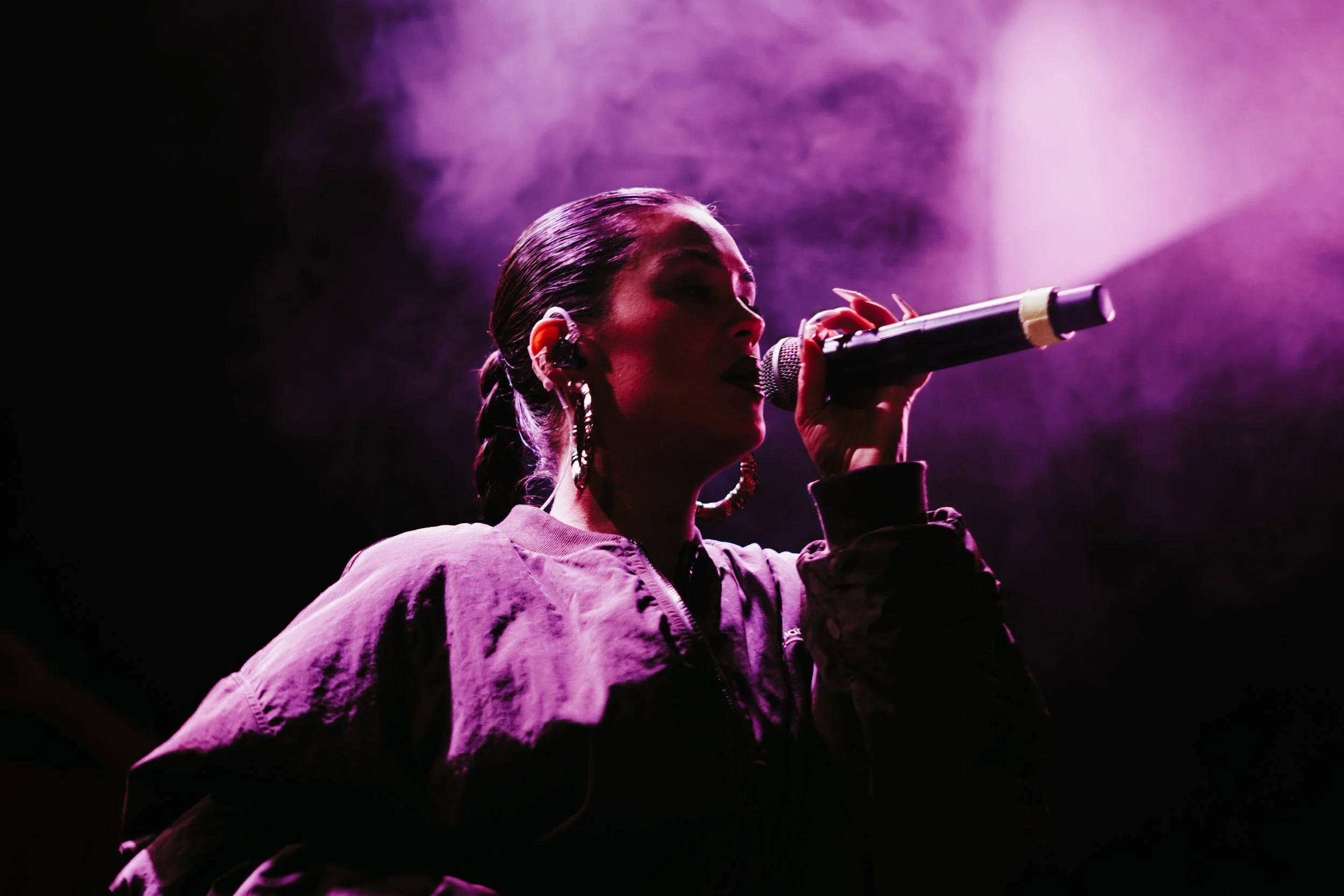 Une femme chante dans l'obscurité avec un éclairage violet, tenant un microphone