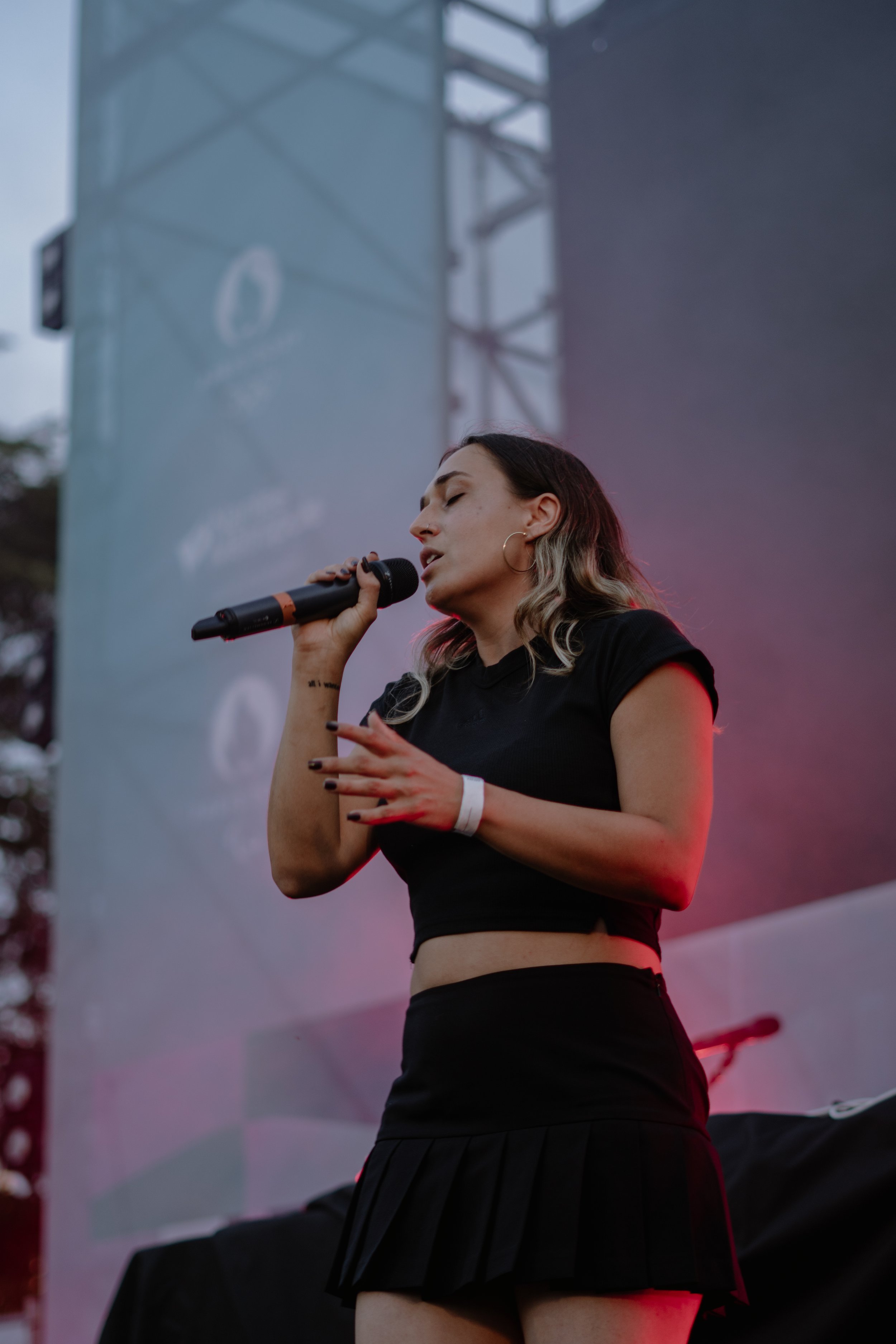 Une femme chante en solo lors d'un concert en plein air, tenant un micro dans la main, avec un grand écran géant en arrière-plan.