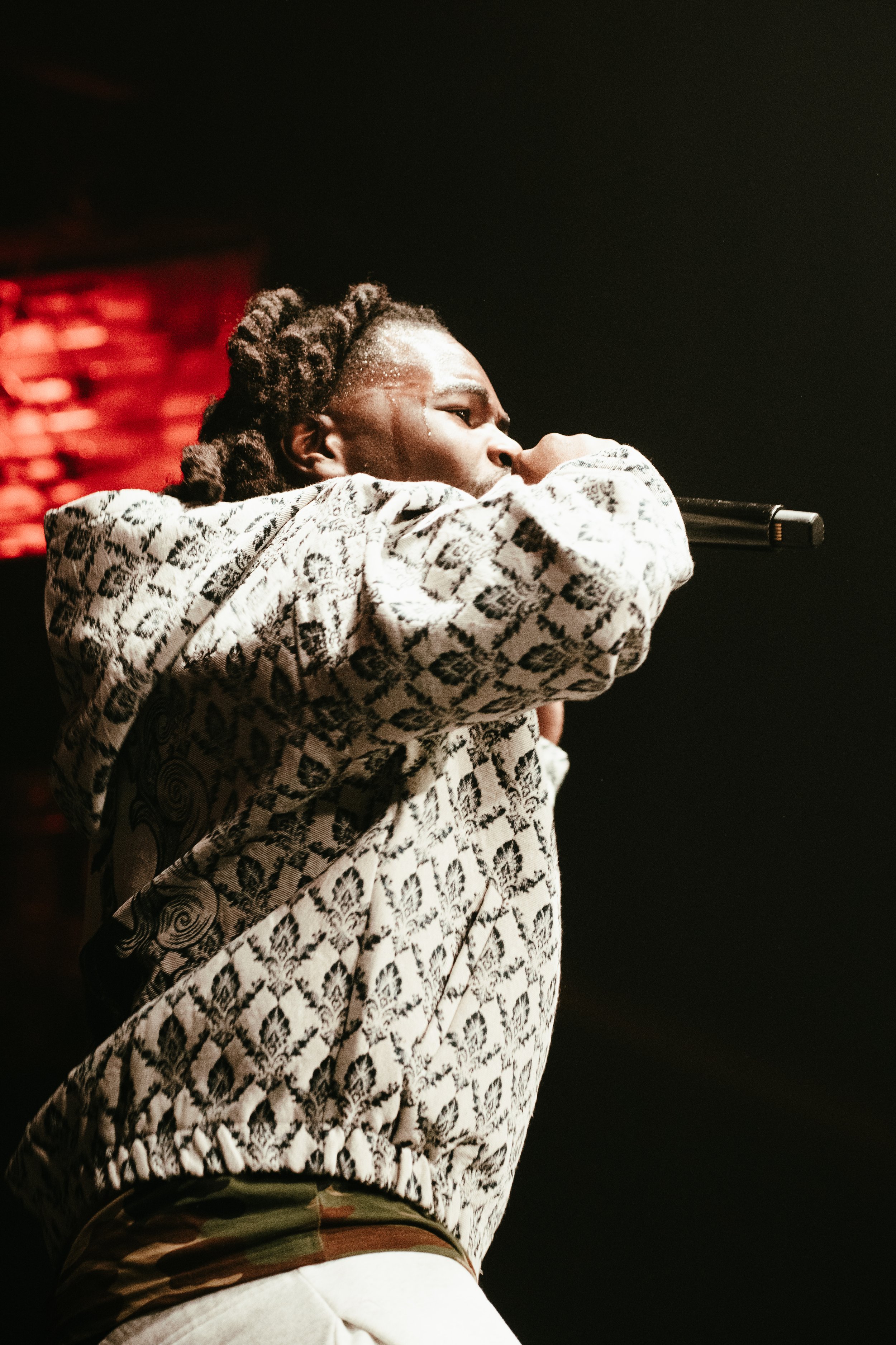 Un artiste en train de chanter ou de performer sur scène, tenant un micro, avec un éclairage sombre et une ambiance de concert.