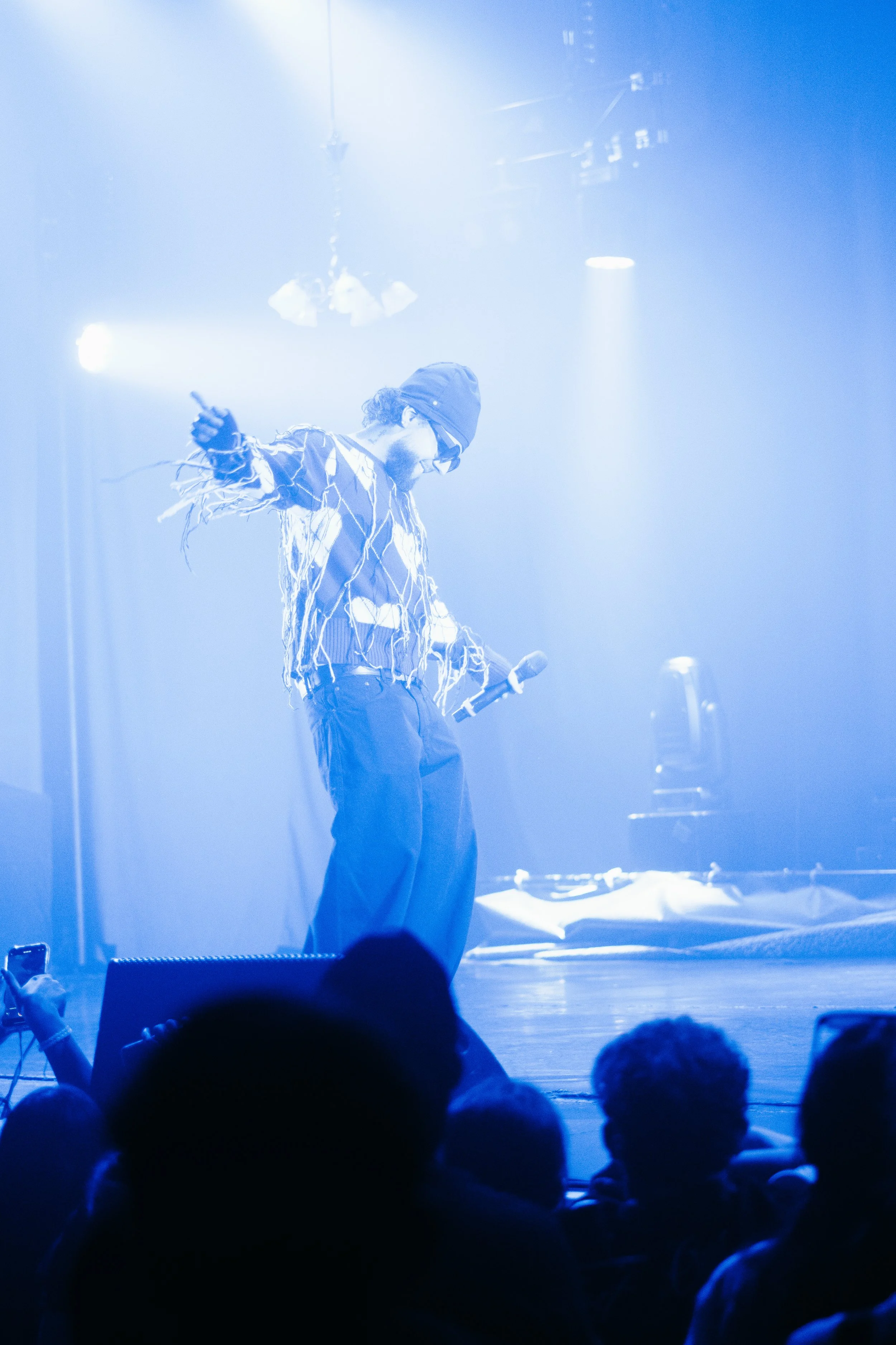 Un homme avec un bonnet et des lunettes, tenant un microphone, en train de faire un spectacle sur scène avec un éclairage bleu.