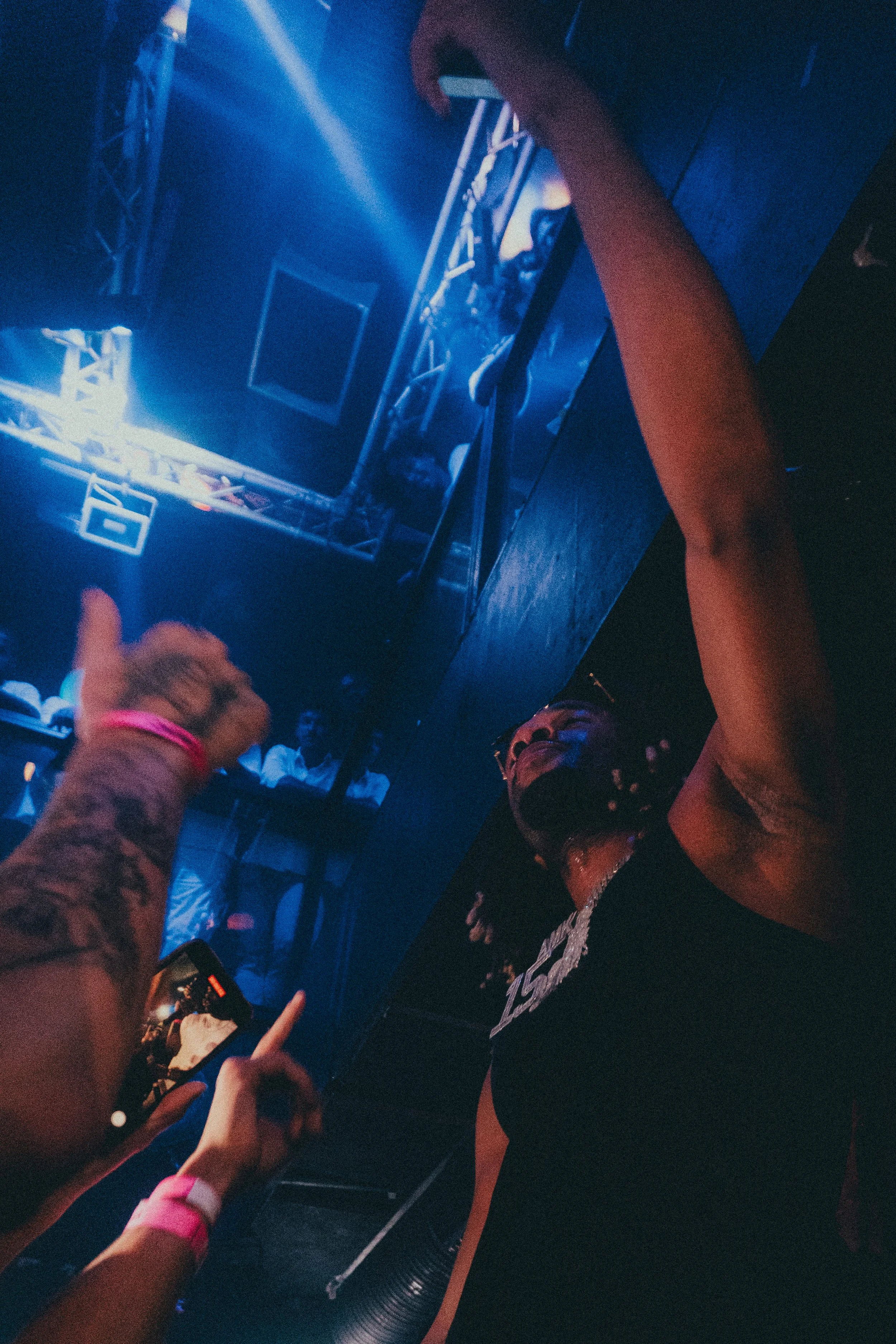 Une personne portant un masque dans une fête ou un club, souriant, entourée d'autres personnes et d'effets lumineux bleus.