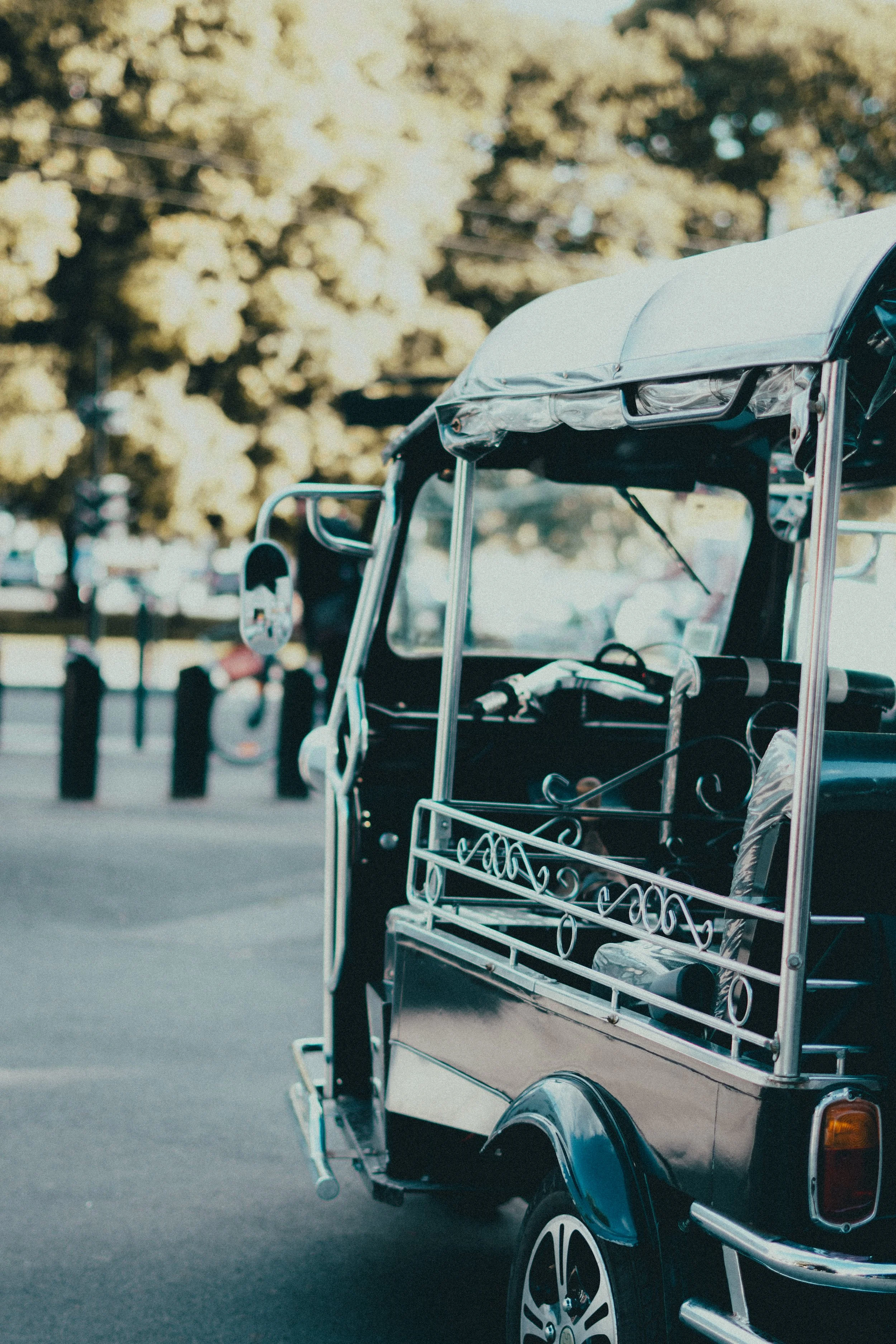 Une pousse-back à trois roues noire avec un toit blanc et une surface en métal décorative à l'arrière, garée dans une rue avec des arbres en arrière-plan