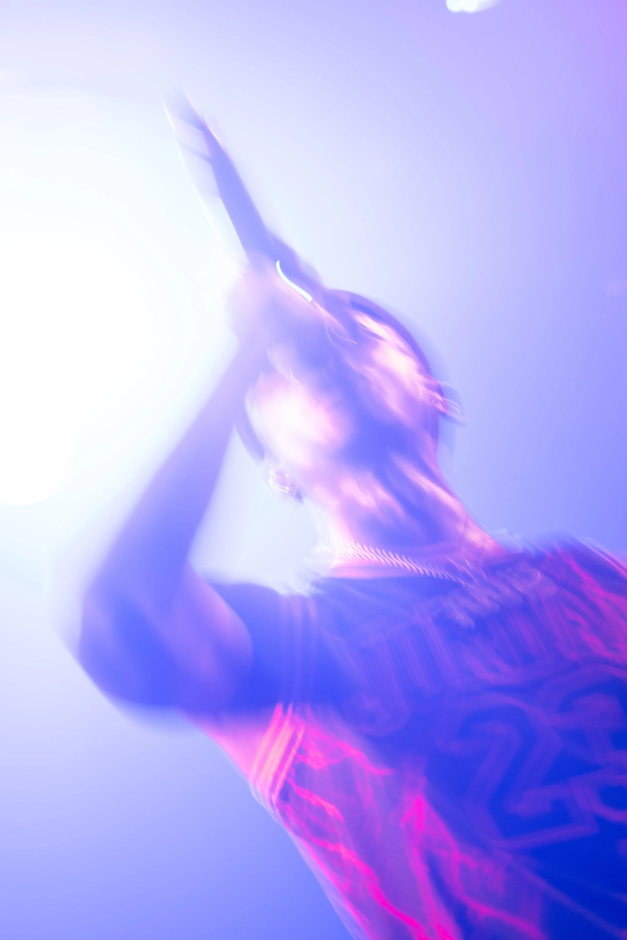 Un chanteur ou rappeur en performance sous des lumières violettes et bleues, dans une atmosphère de spectacle avec un effet flou artistique.