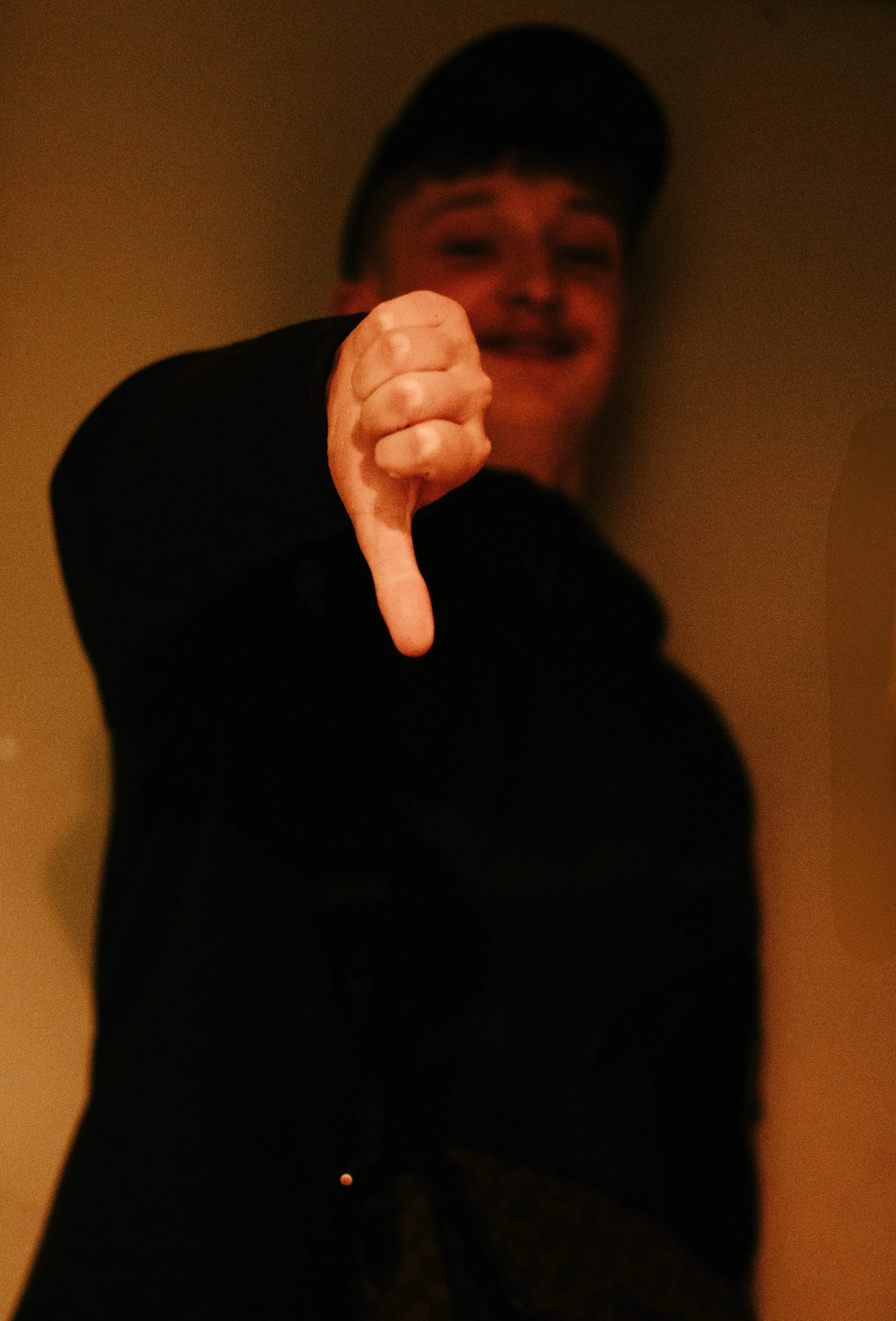 Personne souriante portant une casquette, montrant un pouce vers le bas, dans un environnement intérieur