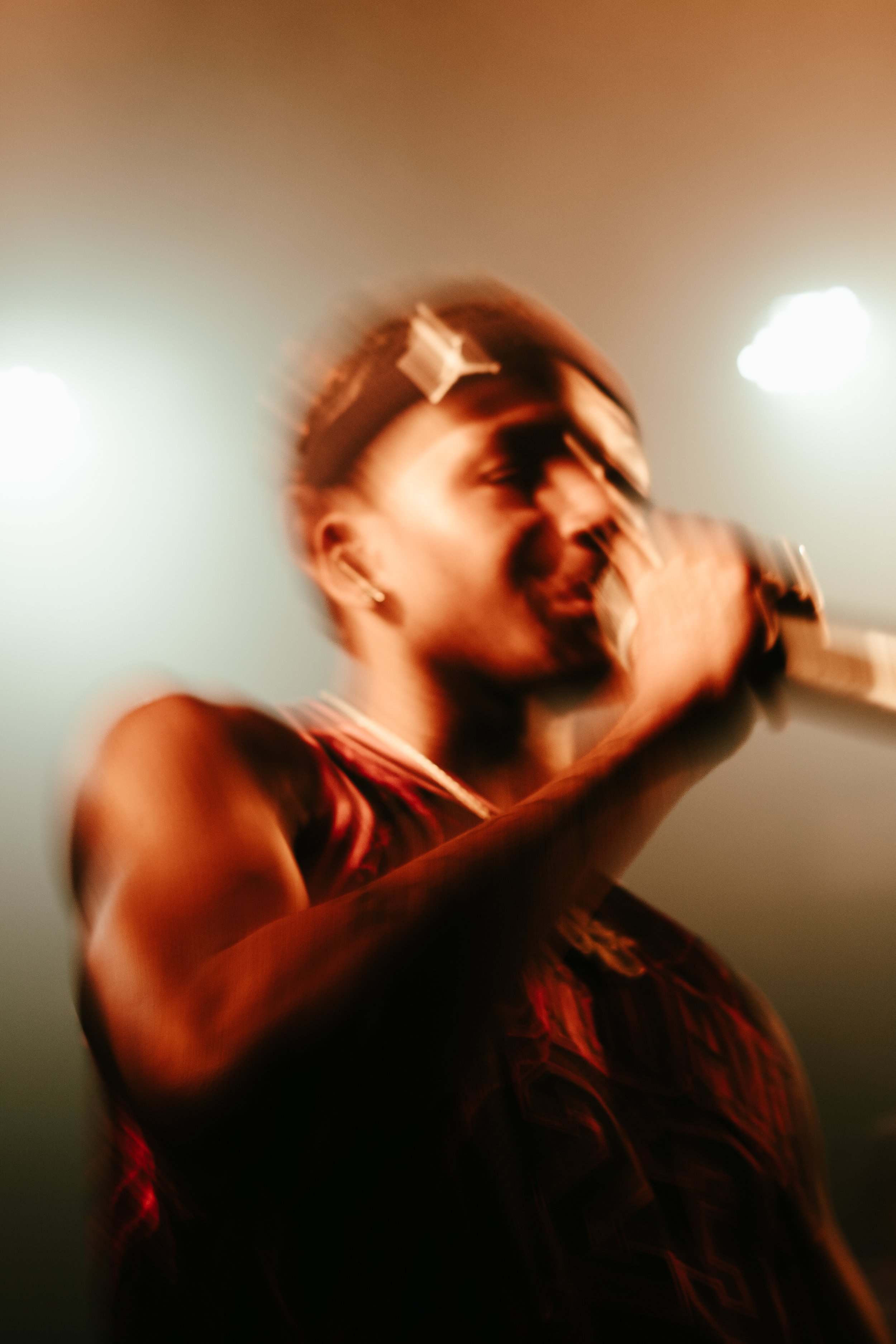 Une personne chante lors d'une performance sur scène, tenant un micro, avec un éclairage de scène en arrière-plan.